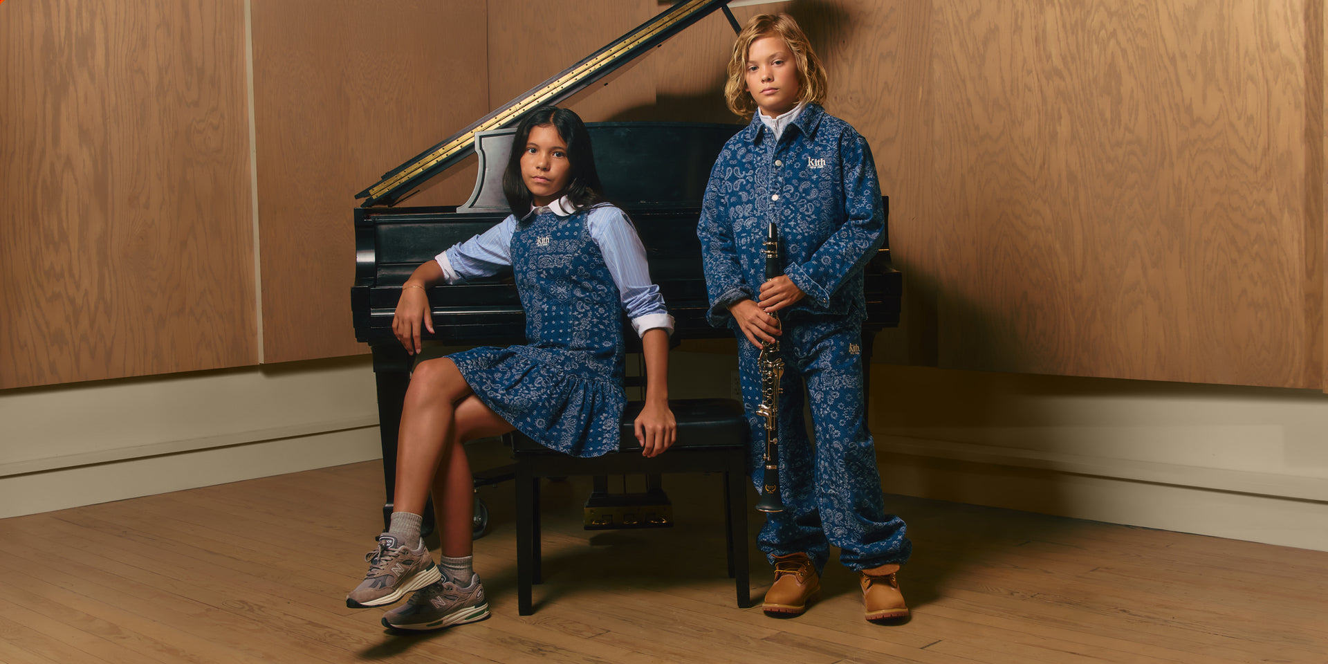 Kith Kids duo at a grand piano: girl in blue bandana-print Kith denim pinafore, boy in matching denim set holds a clarinet