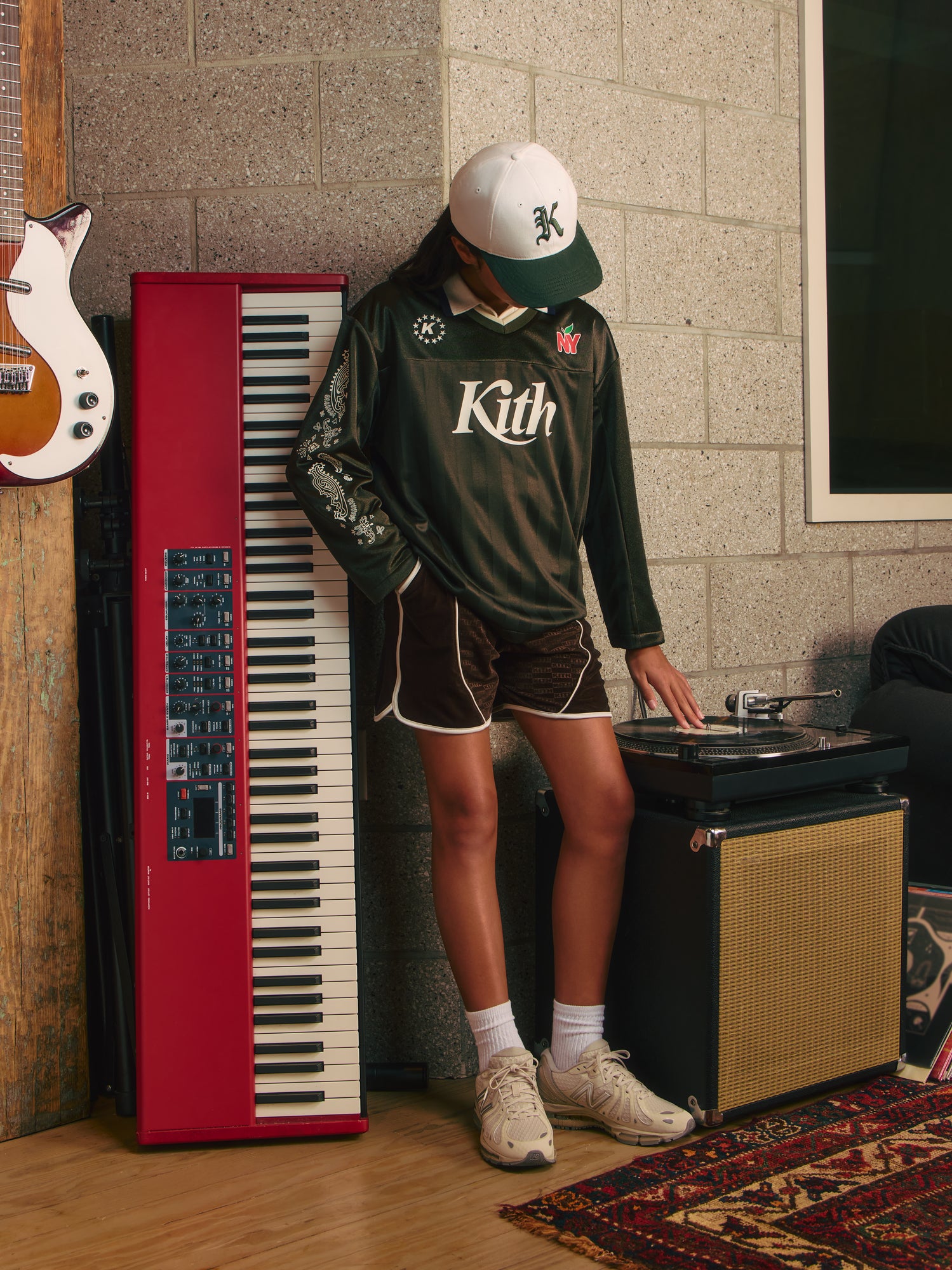 Kith Kids girl in white Kith K cap and green Kith New York soccer jersey cues a turntable in a music room