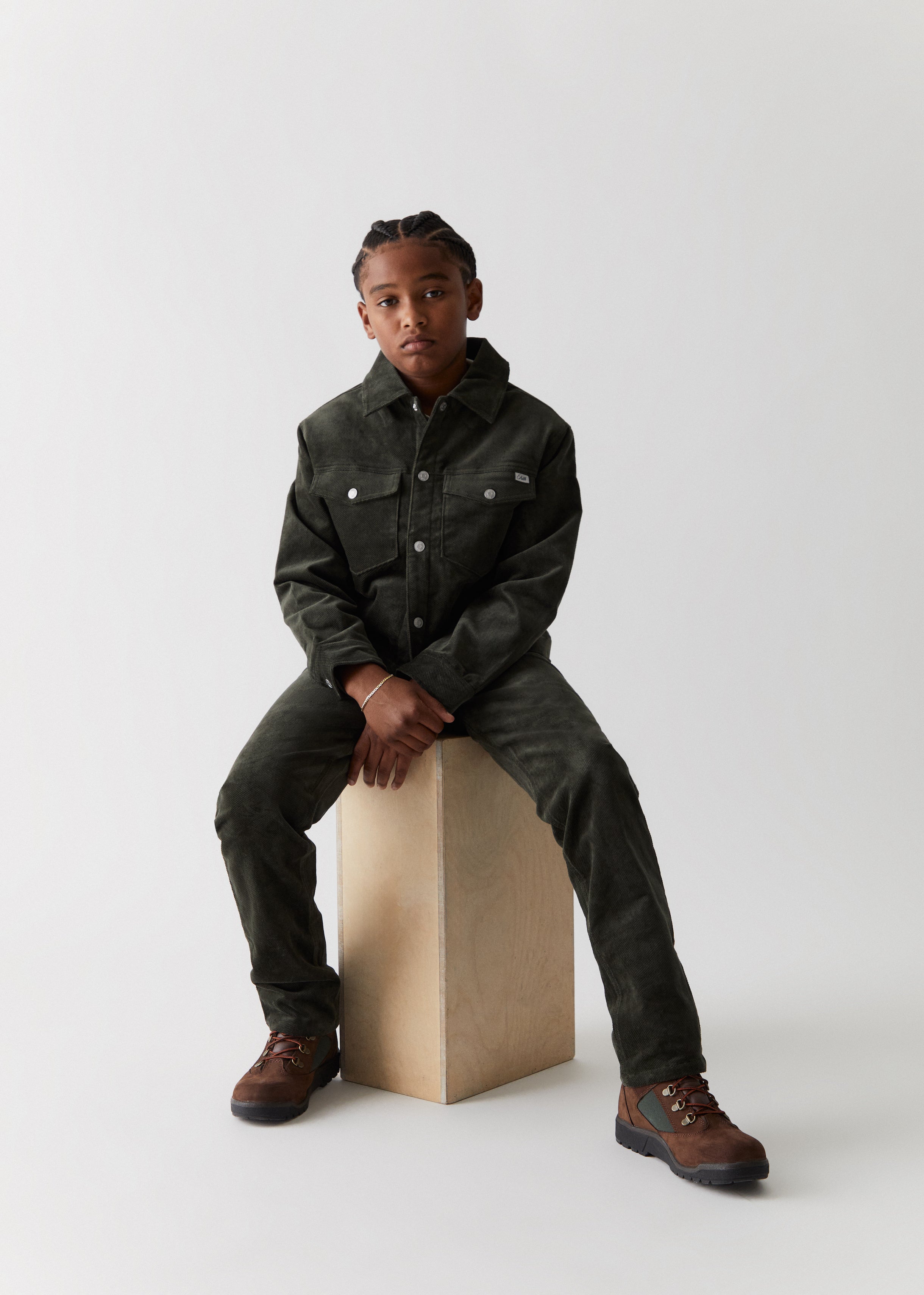 A child wearing an army green denim jacket and matching denim pants from the Kith Kids Fall Classics 2023 collection.