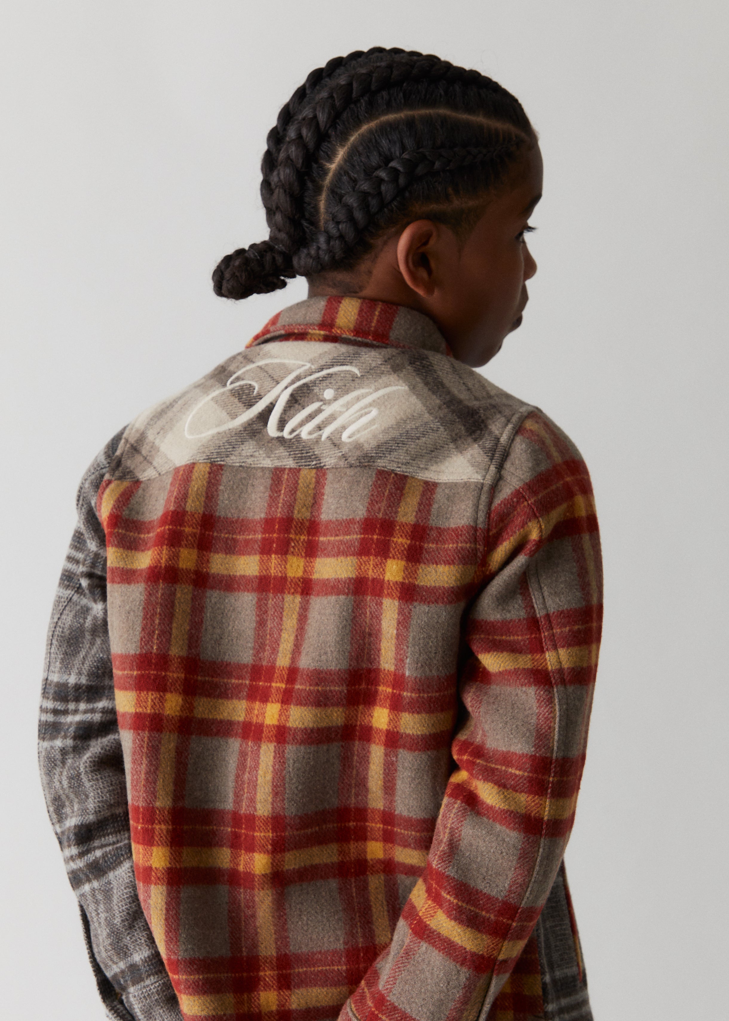 A child facing backwards, showcasing a red flannel shirt with Kith script embroidery across the back from Kith Kids Fall Classics 2023.
