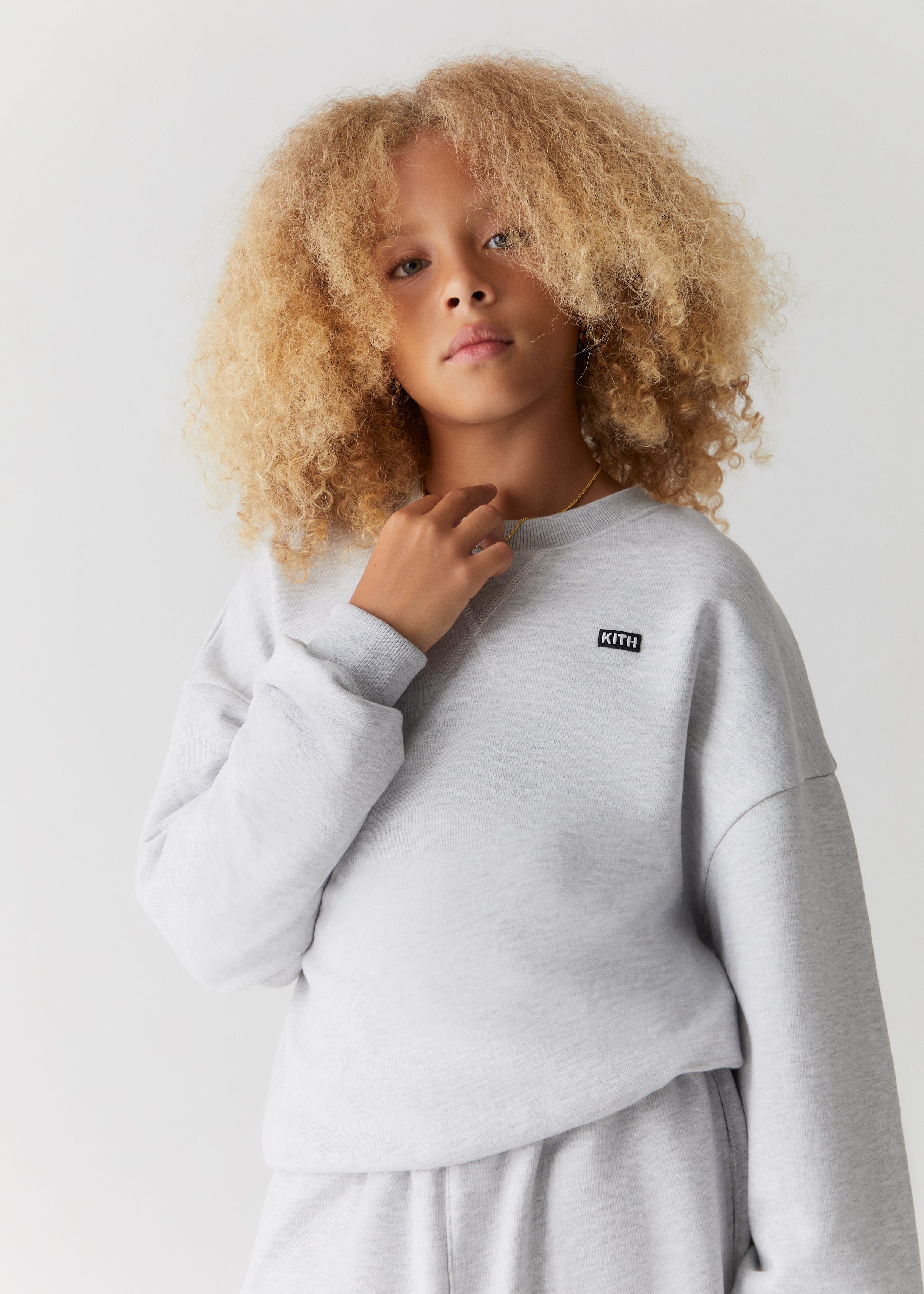 A child wearing a grey Kith-branded crewneck from the Kith Kids Fall Classics 2023 collection.