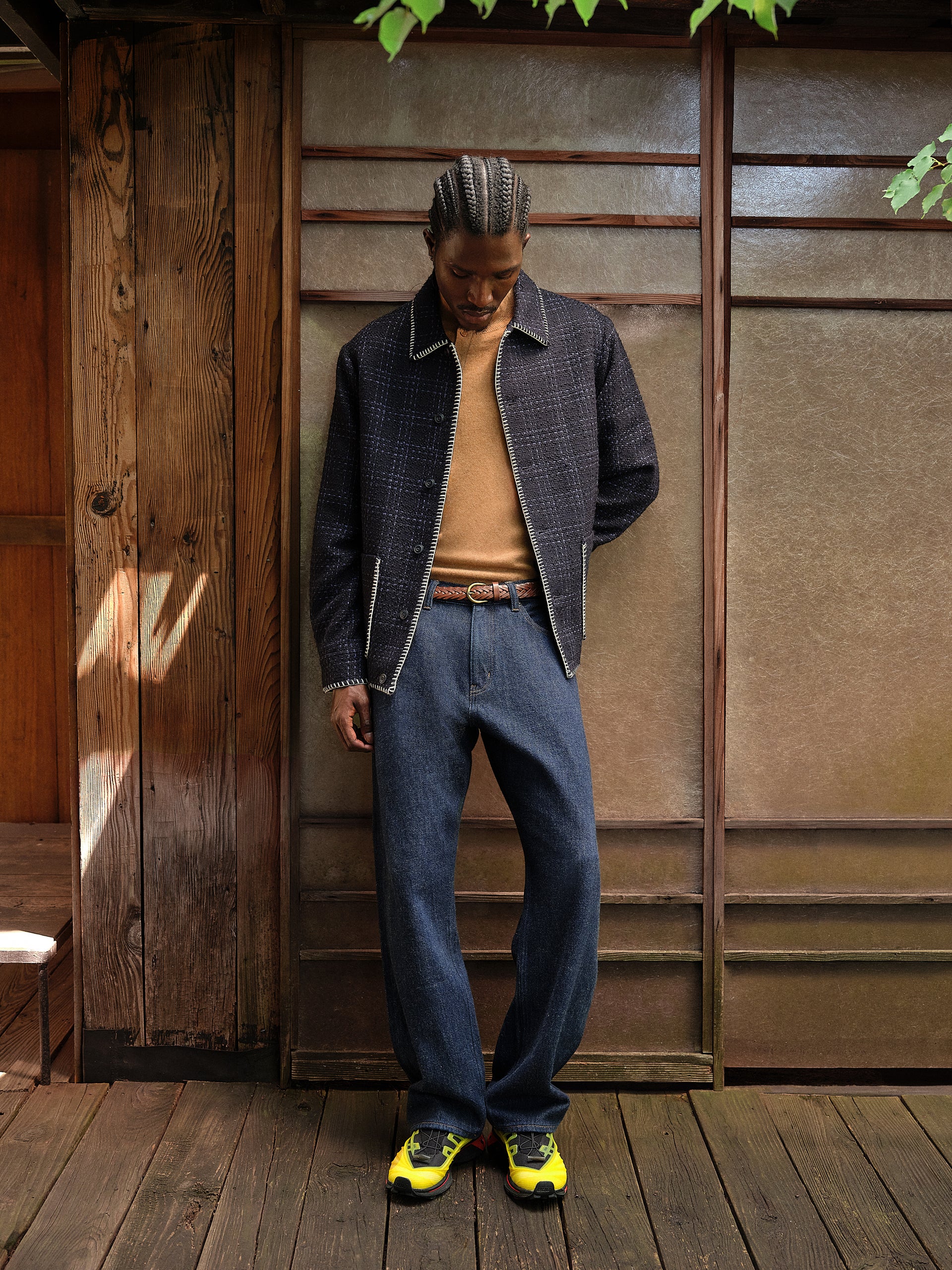 Model in a navy blanket-stitch tweed jacket, camel sweater and dark jeans with yellow trail sneakers by a shoji screen