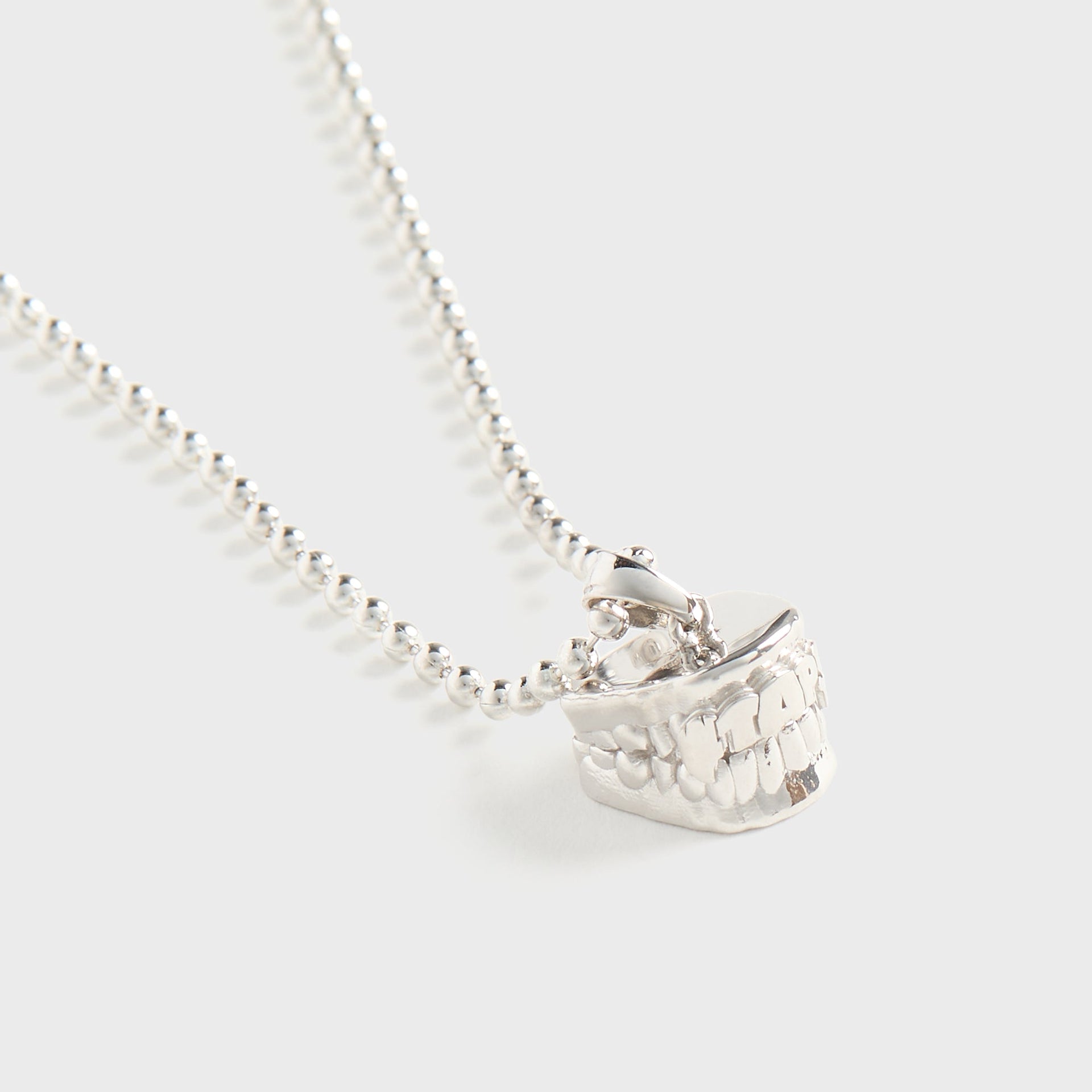 WTAPS x Grillz Jewelz Vamp silver necklace, close-up of pendant showing carved teeth detail and WTAPS lettering