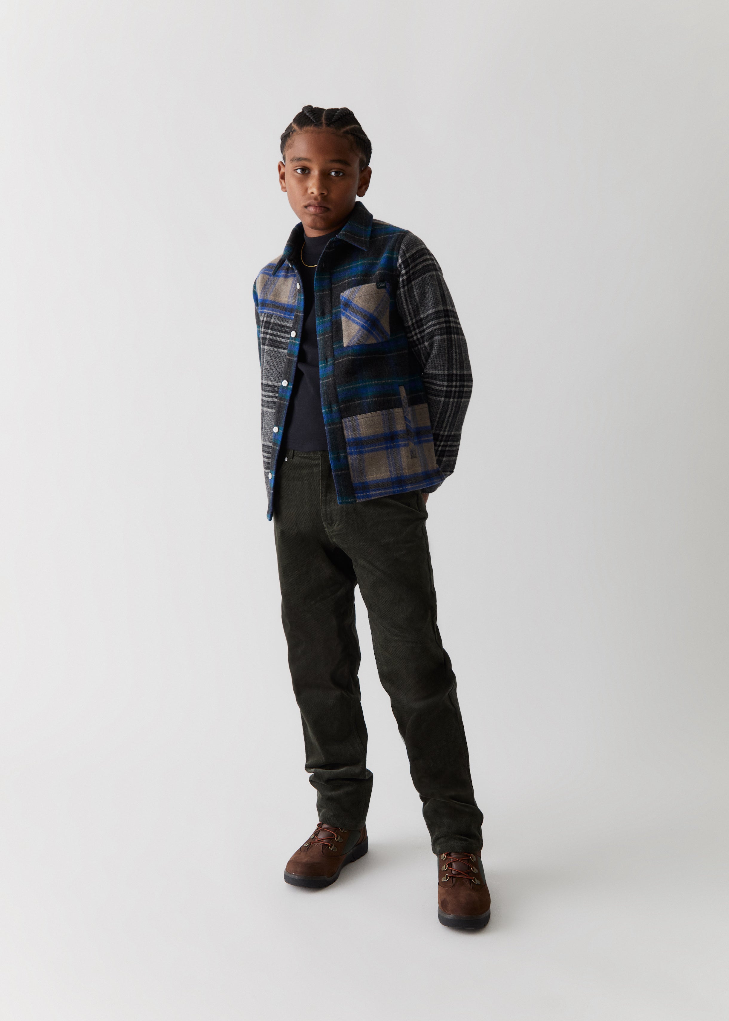 A child wearing a blue and grey color-blocked flannel, along with black jeans from the Kith Kids Fall Classics 2023 collection.