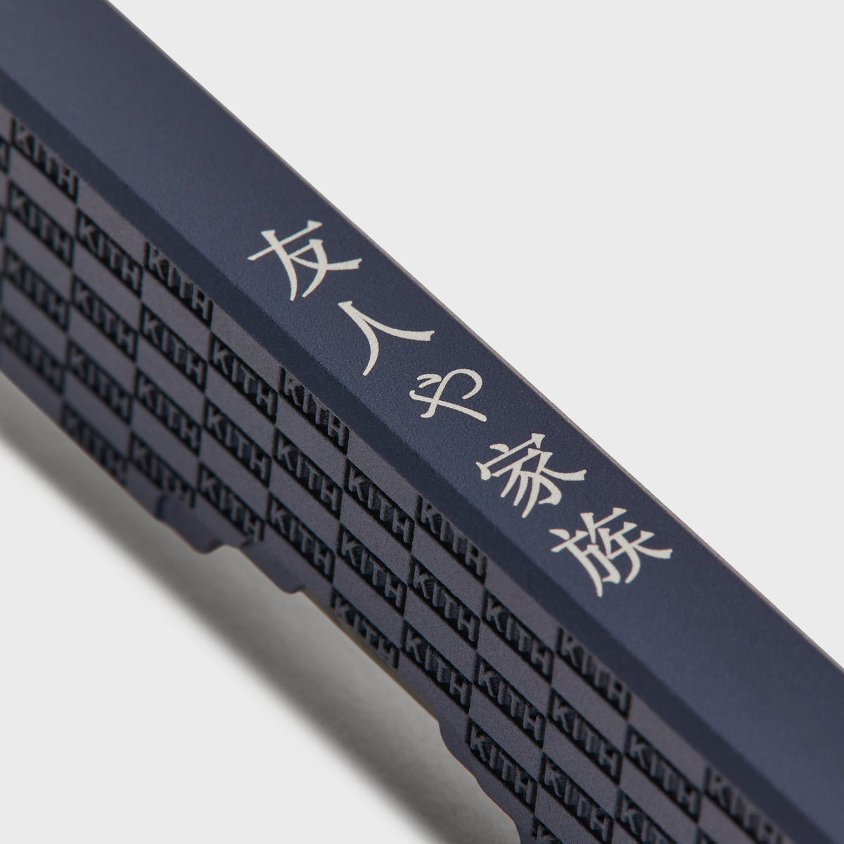 Macro detail of the KITH checkerboard engraving on the Kith x Benchmade Yamori Nocturnal knife's navy titanium handle