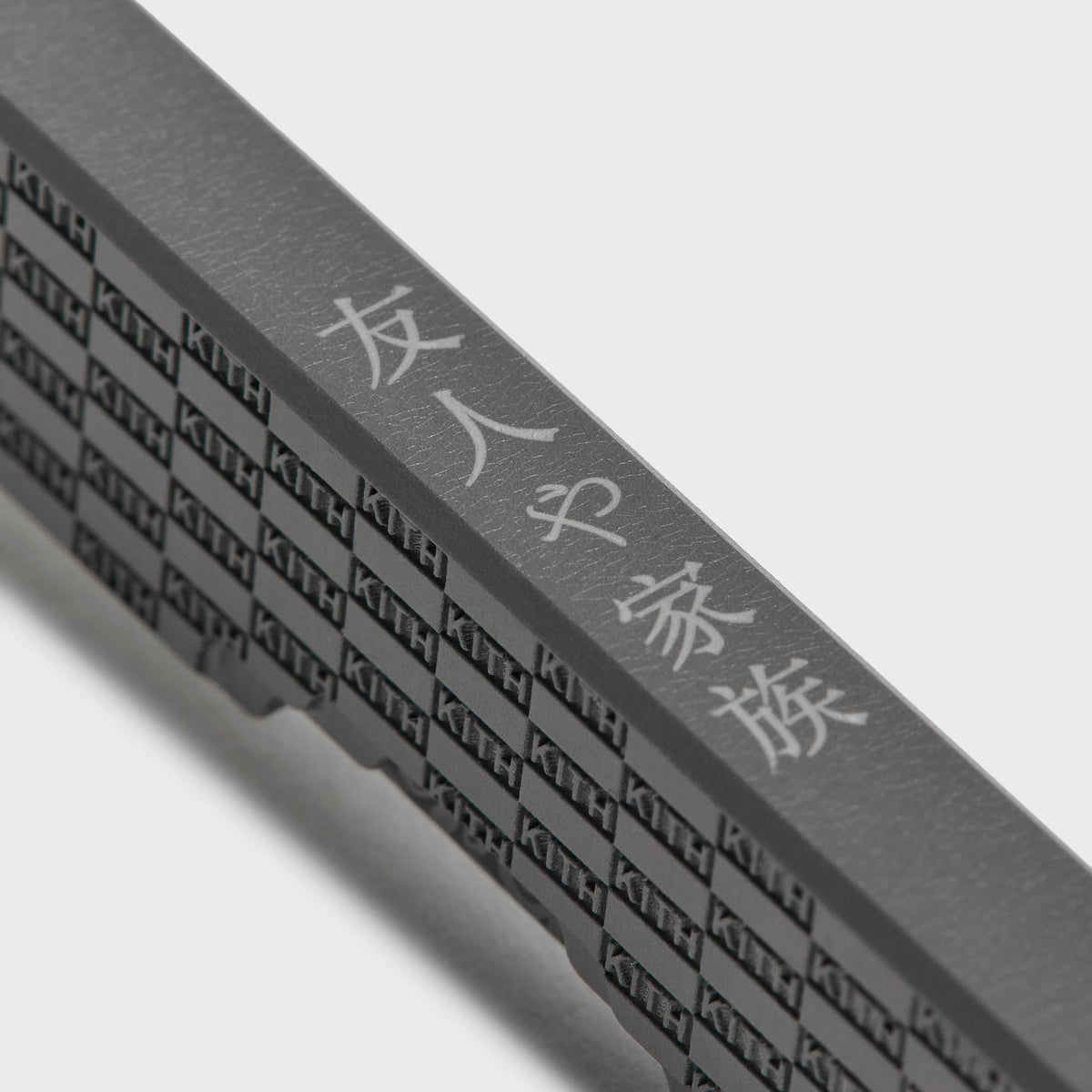 Close-up of the Kith x Benchmade Yamori Drift knife's spine, etched kanji lettering beside the KITH checker pattern