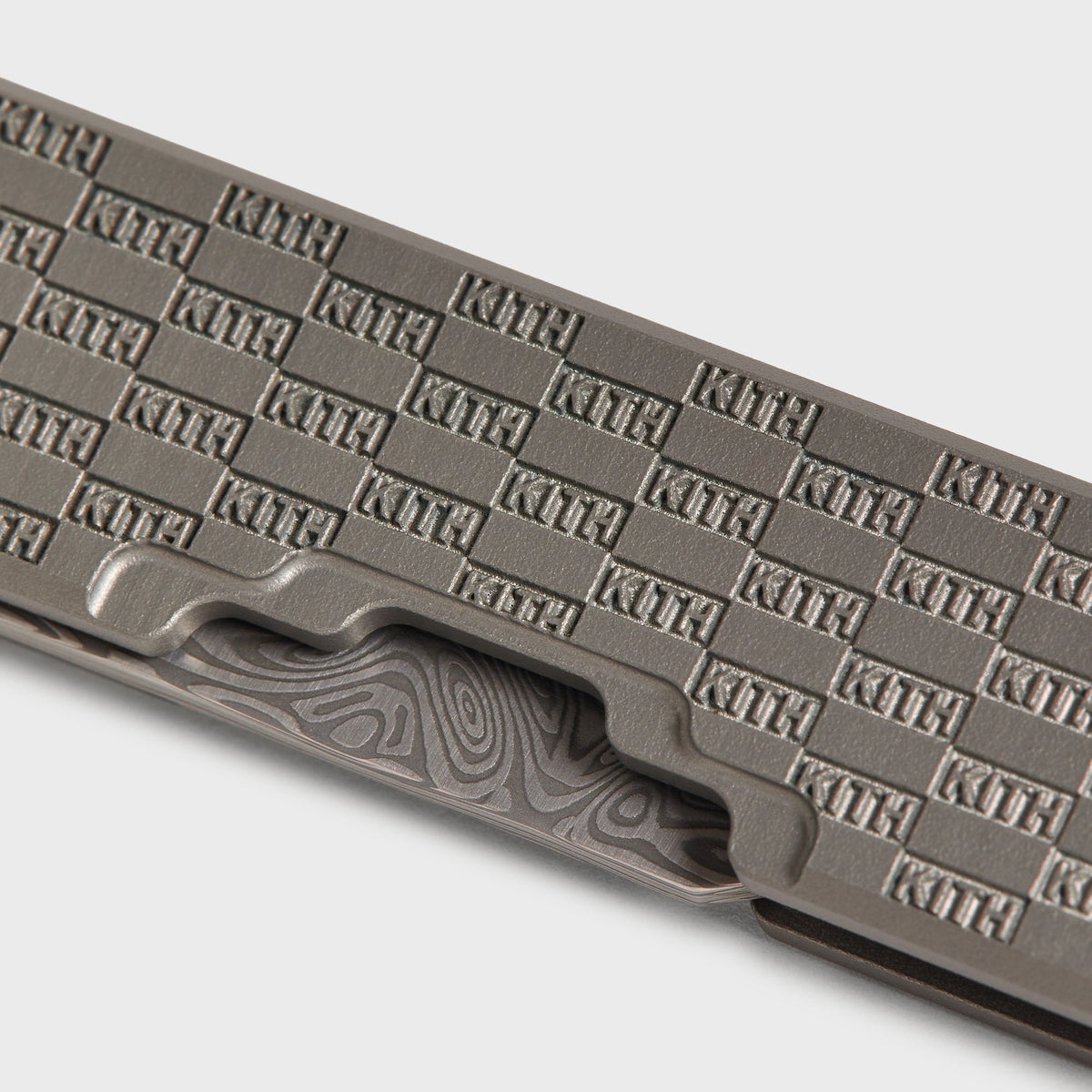 Macro detail of the KITH checkerboard engraving on the Kith x Benchmade Yamori Drift knife's gunmetal grey handle