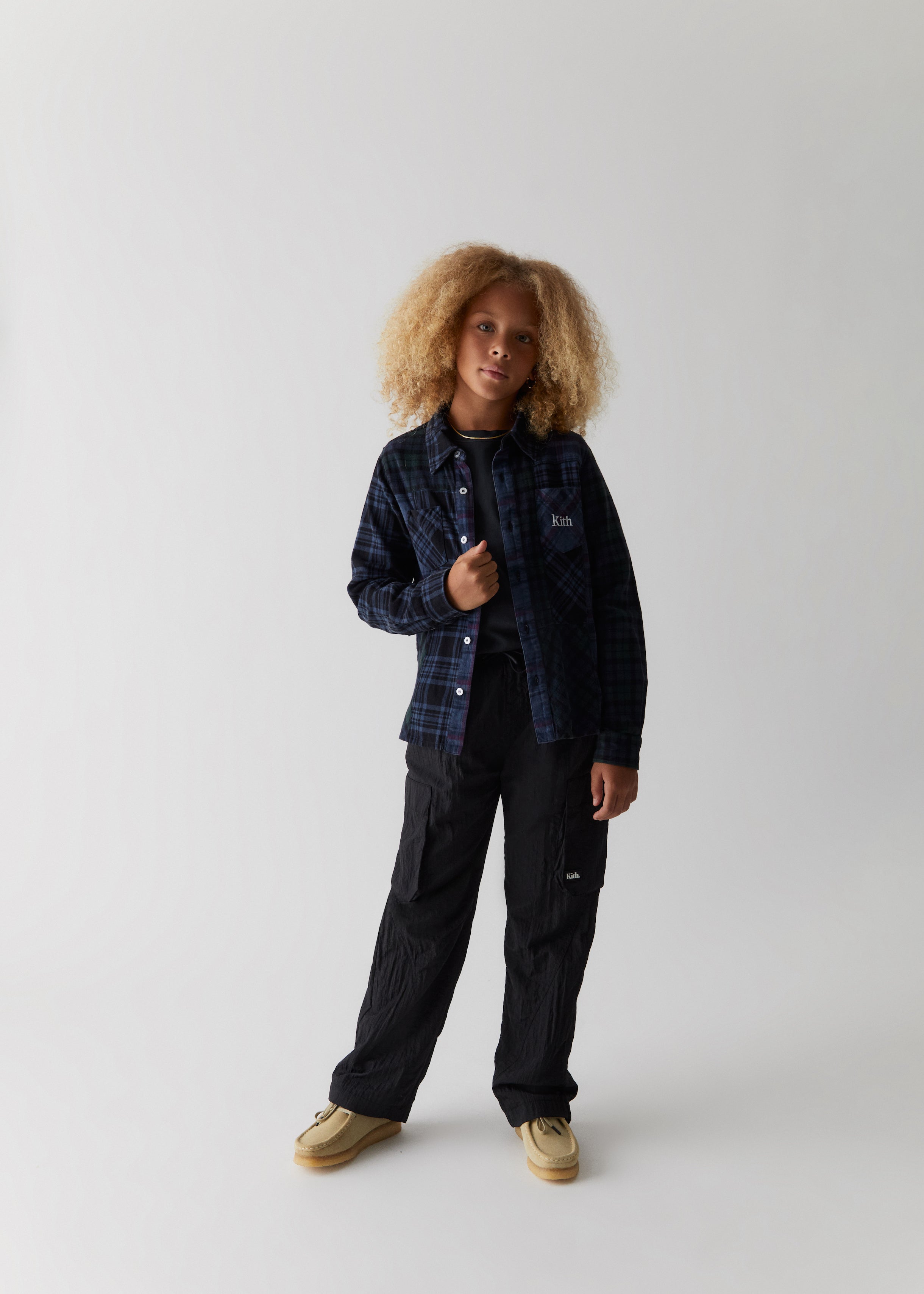 A child wearing a blue flannel and black cargo-style sweatpants from the Kith Kids Fall Classics 2023 collection.