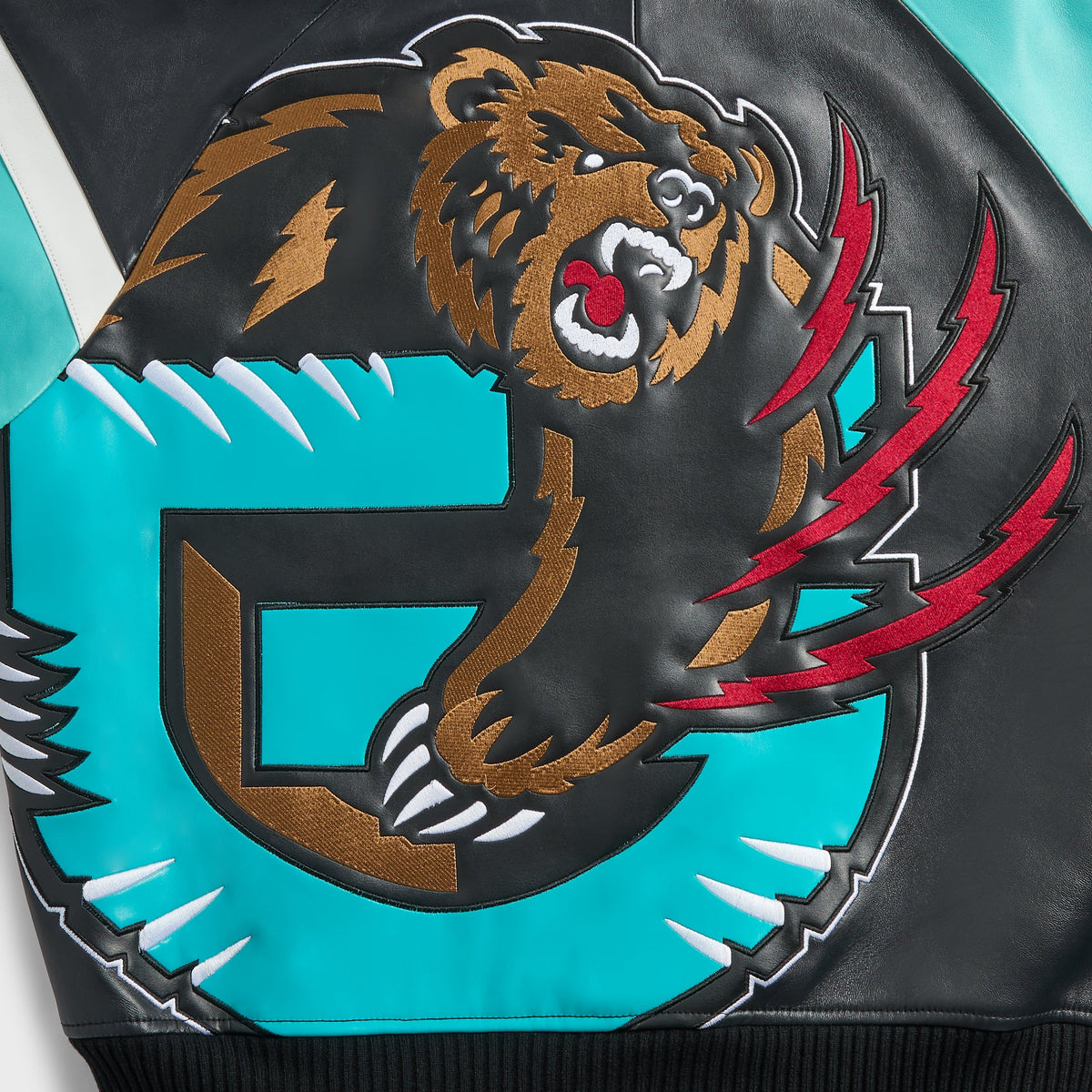 Close-up of embroidered Grizzlies bear and teal G logo on the back of the black and teal Kith & AVIREX leather jacket