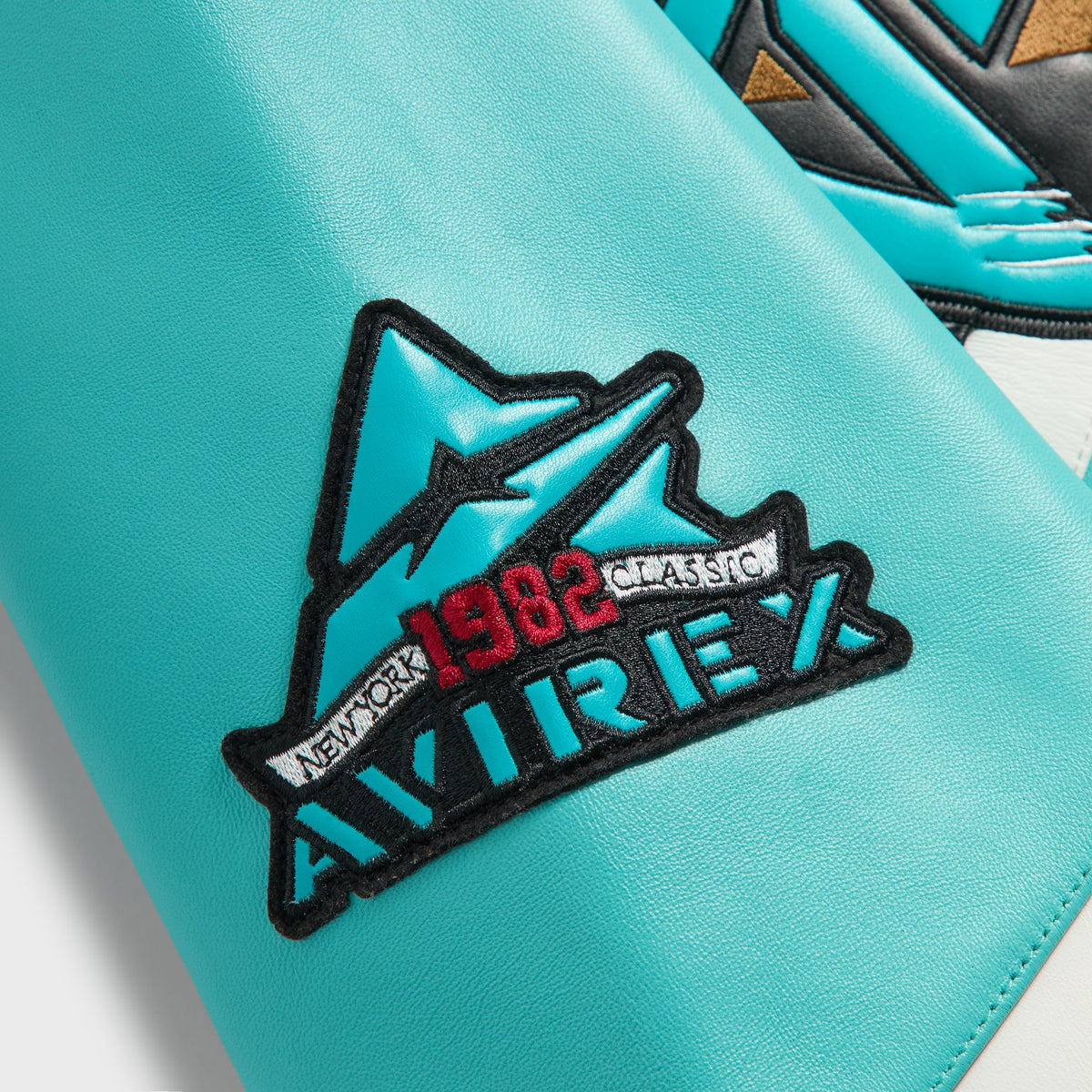 Close-up of AVIREX 1982 New York Classic mountain patch on the teal leather sleeve of the Kith Grizzlies jacket