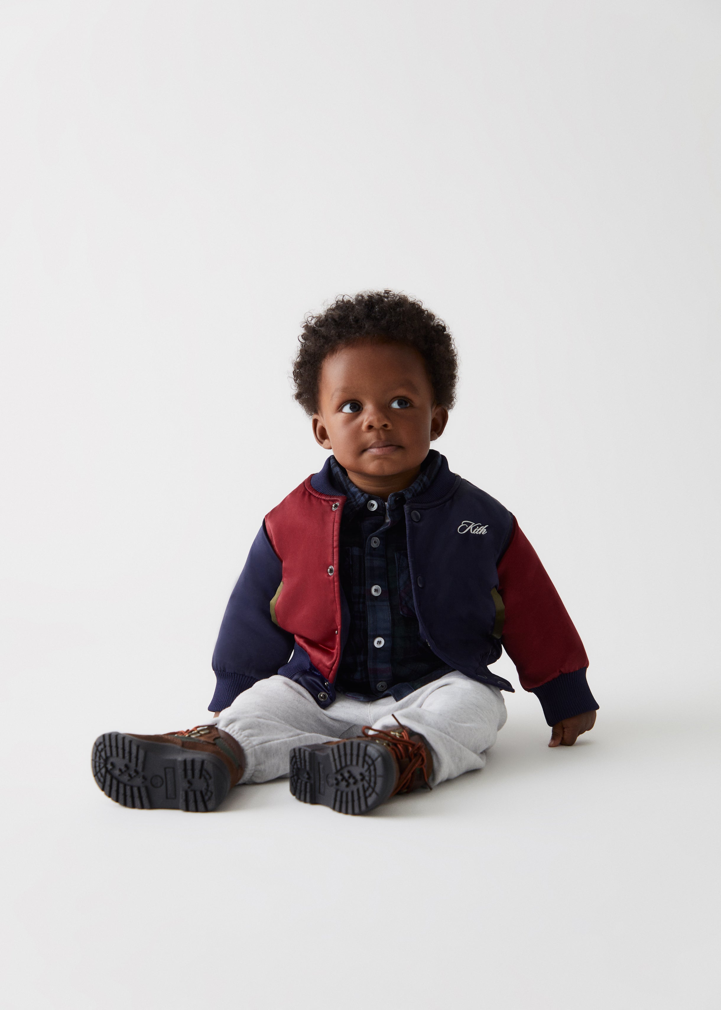 A baby wearing a color-blocked Kith varsity jacket and grey sweatpants.