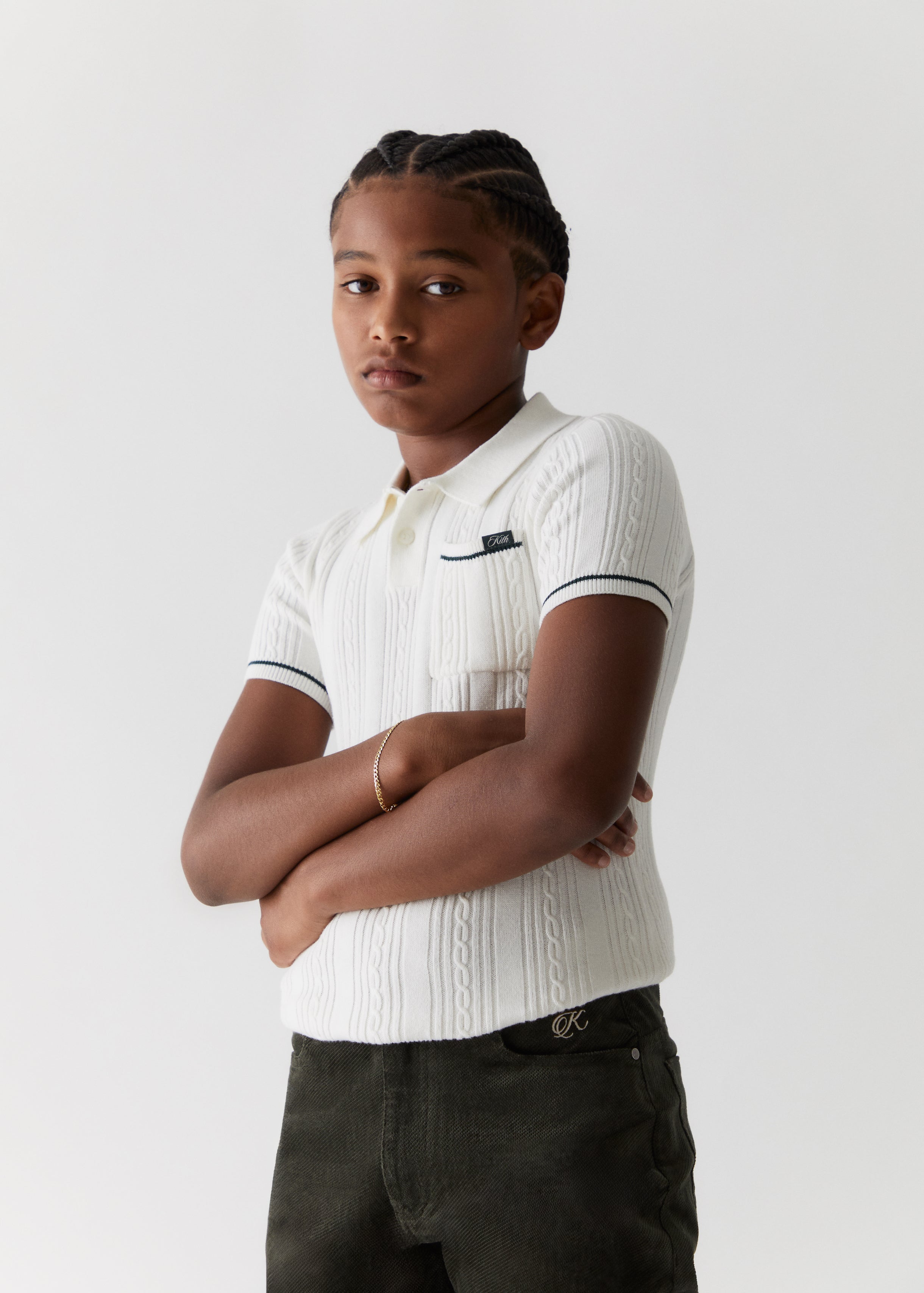 A child wearing a cable knit white polo from the Kith Kids Fall Classics 2023 collection.