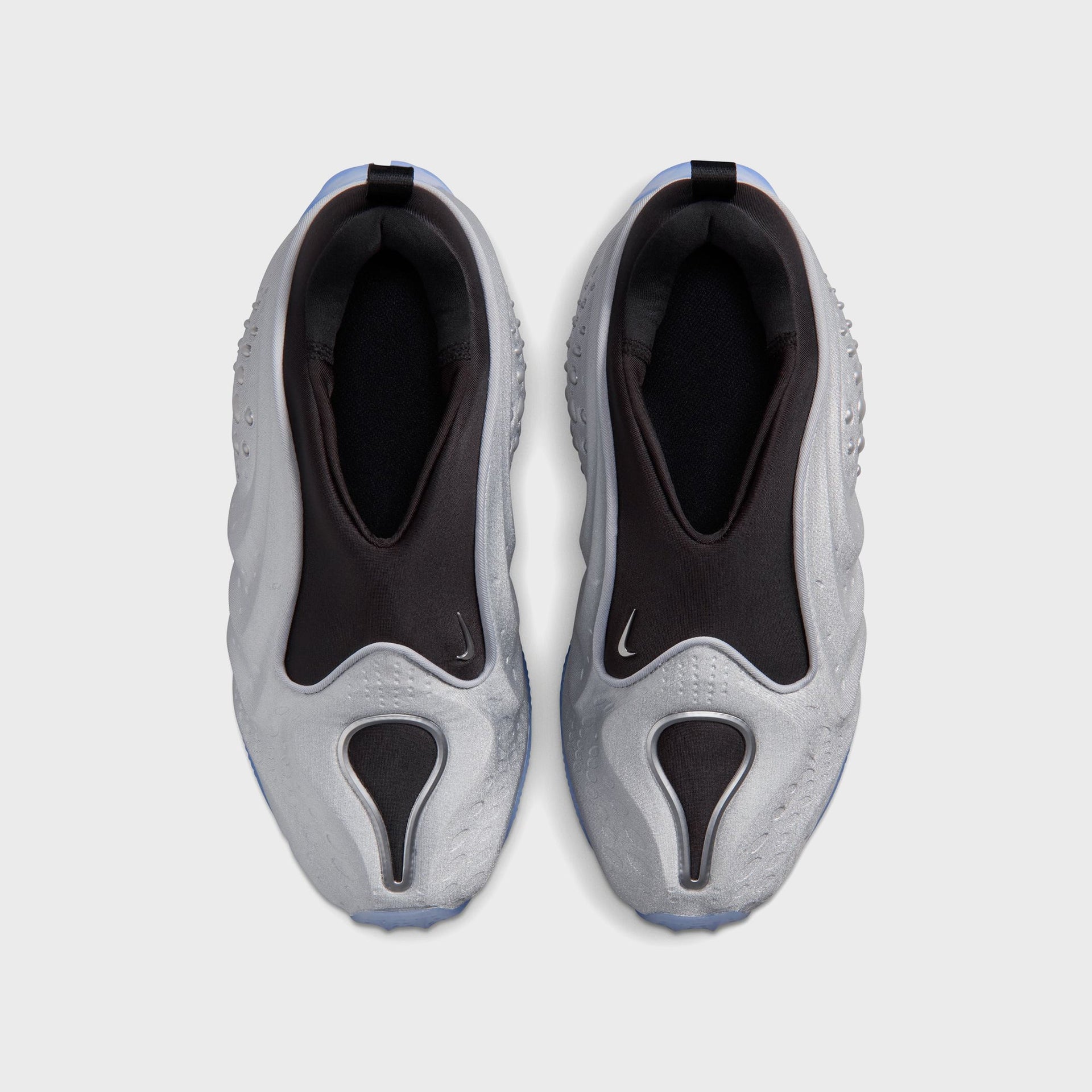 Nike WMNS First Sight Shadow Metallic Silver, top-down view of the slip-on pair with black collars and silver swoosh toe windows