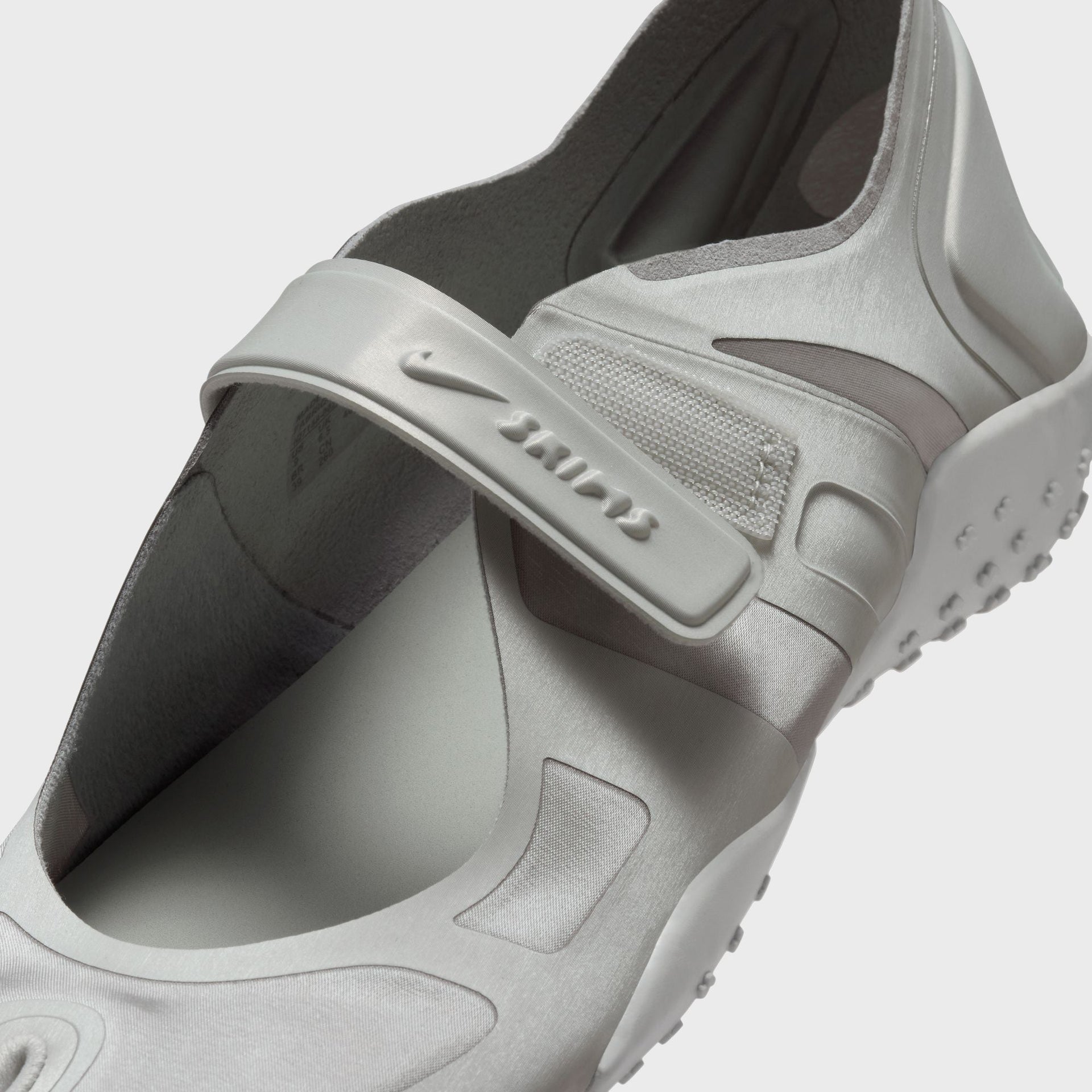 Close-up of the NikeSKIMS Rift Satin strap in Night Silver showing the Nike Swoosh, embossed SKIMS logo and satin-textured upper
