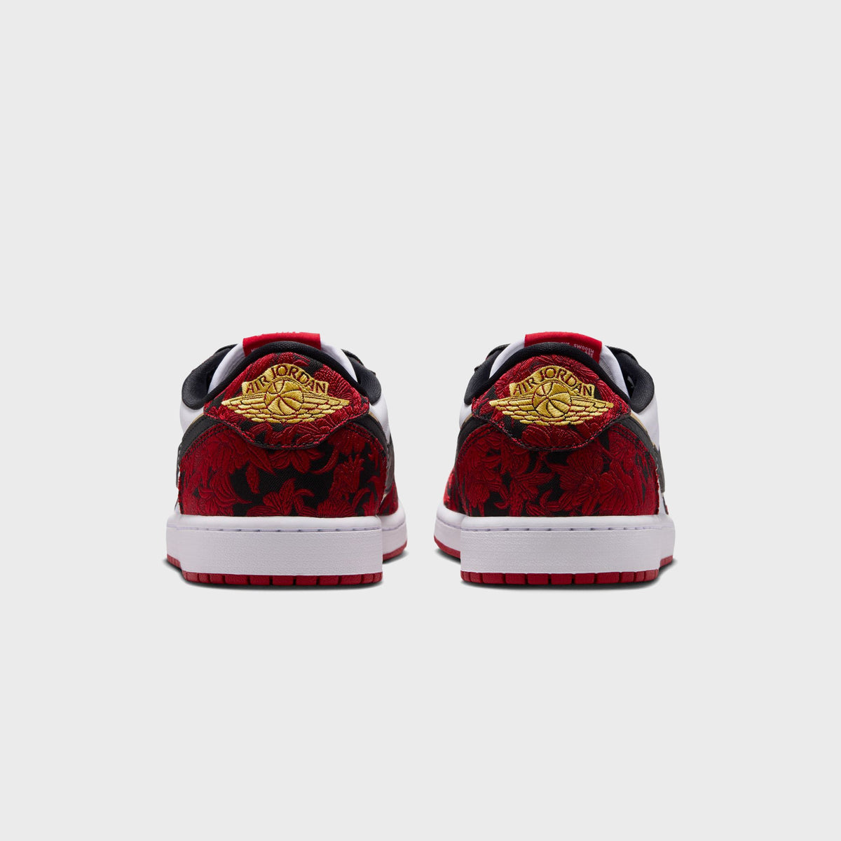 Heel view of Air Jordan 1 Low OG pair showing gold-embroidered Air Jordan wings logo on red floral heel tab and red rubber outsole