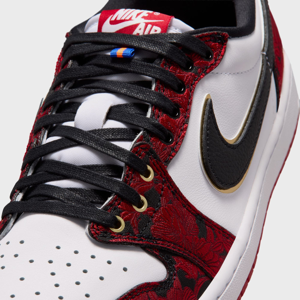 Close-up of Air Jordan 1 Low OG toe box and lacing with black laces, gold eyelets, and red-and-black floral embroidered overlay