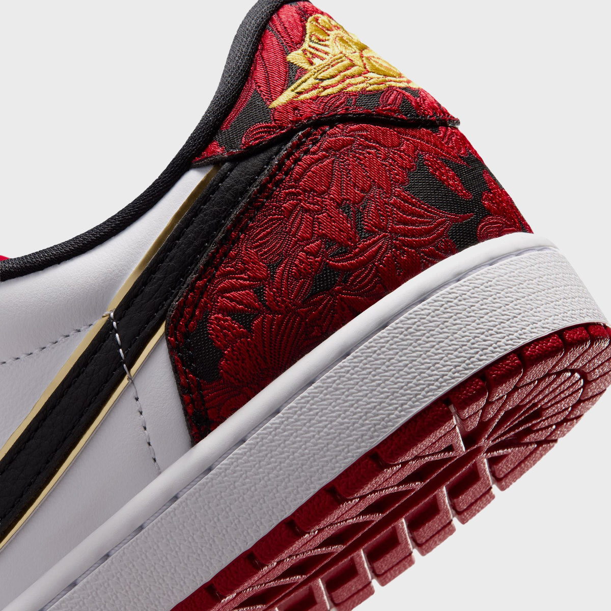 Macro detail of Air Jordan 1 Low OG heel tab showing gold-thread Air Jordan wings logo embroidered on red floral fabric