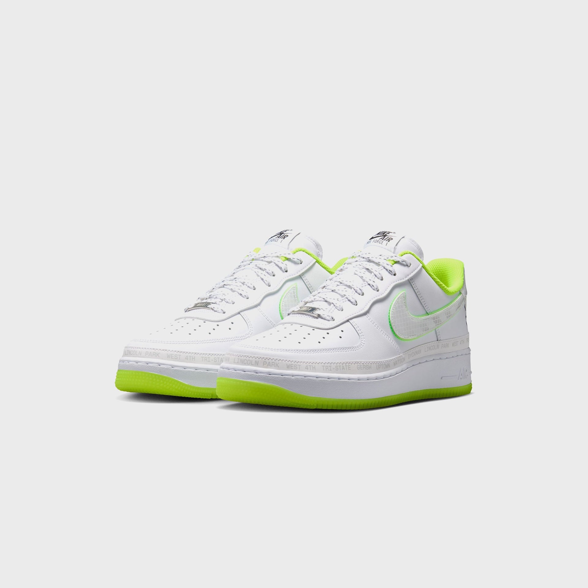 Nike Air Force 1 '07 pair in white with volt collars and soles, front three-quarter angle showing reflective laces and translucent grid Swooshes