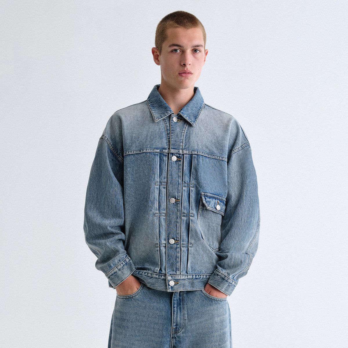 Man wearing a light blue Kith denim trucker jacket and matching jeans against a grey backdrop