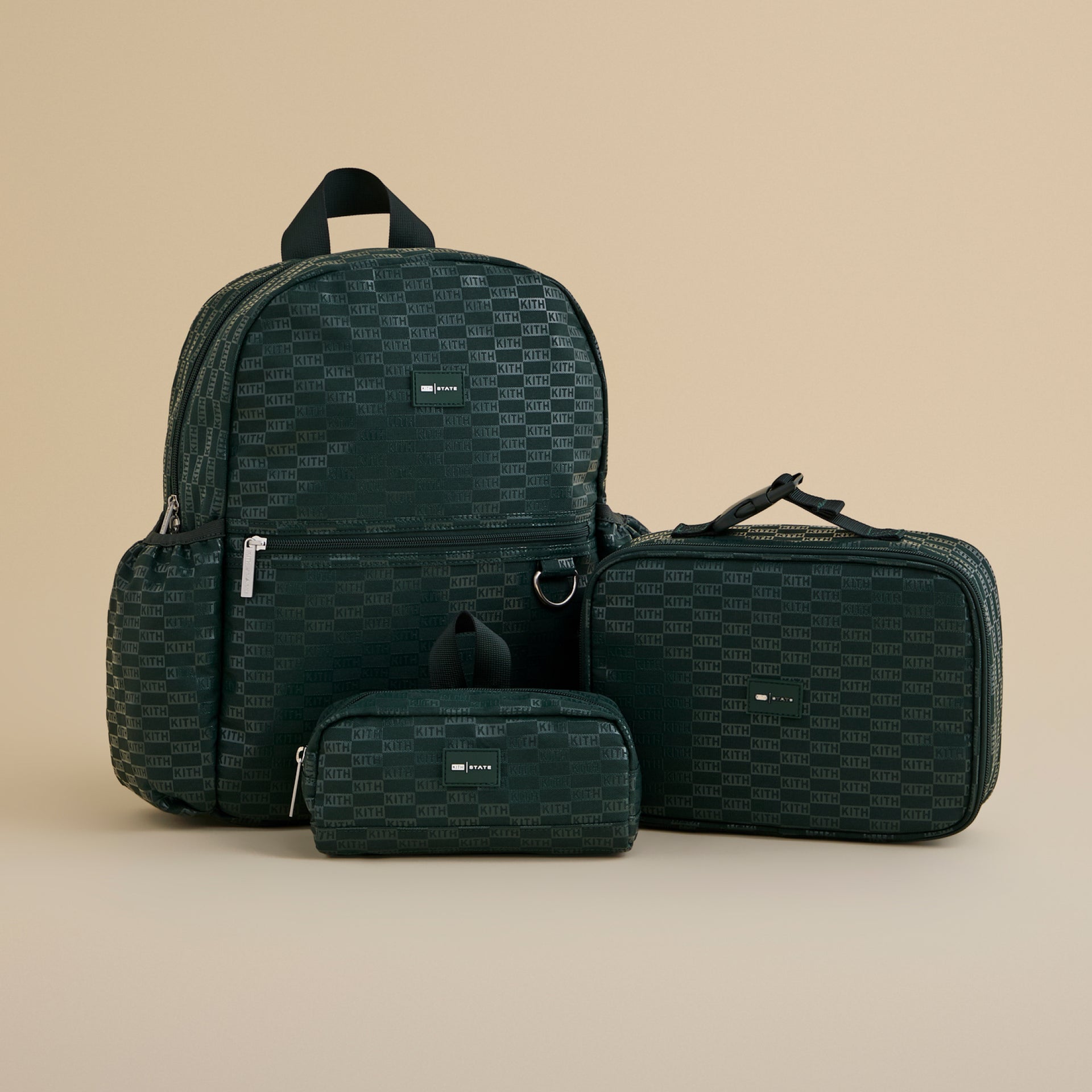 Three dark green Kith State bags in allover KITH check jacquard: a backpack, travel case and zip pouch on a tan background
