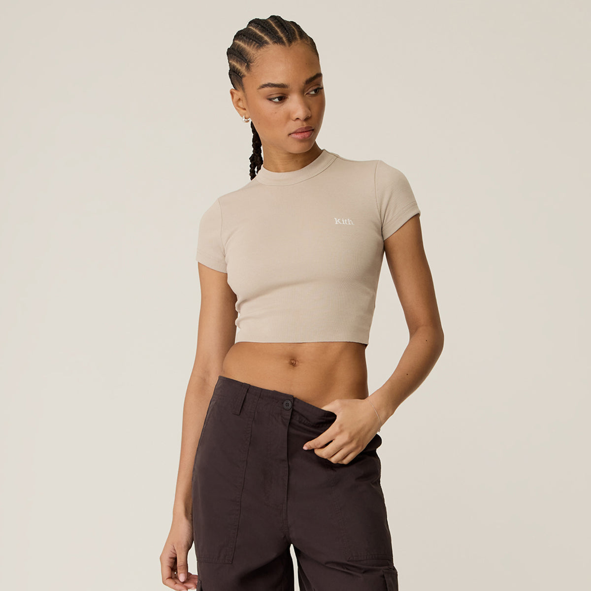 Model wearing a taupe cropped Kith t-shirt with dark brown trousers in a studio setting