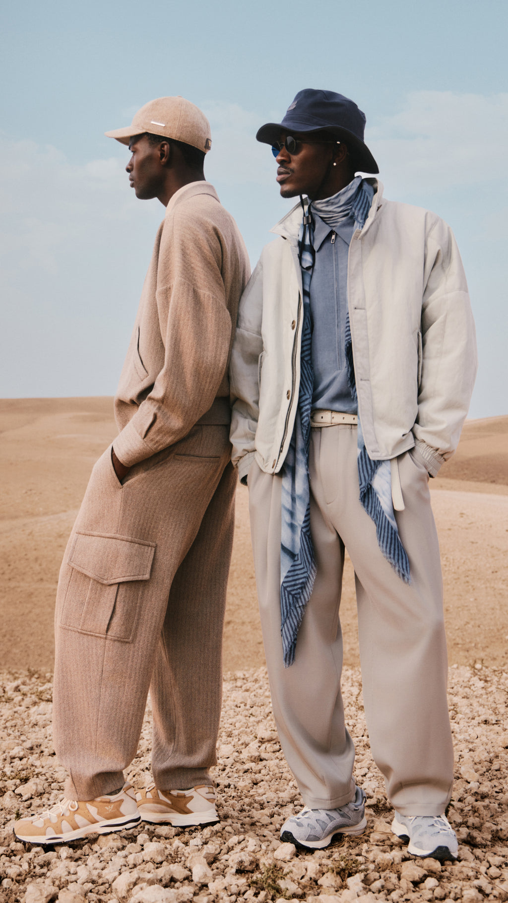 Kith x Giorgio Armani campaign: two models in neutral knit and nylon outerwear, cargo pants and sneakers on rocky desert ground
