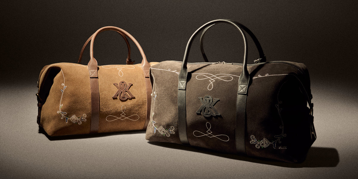 Two Kith suede weekender duffel bags in tan and taupe with embroidered monogram crest and leather handles, close three-quarter view