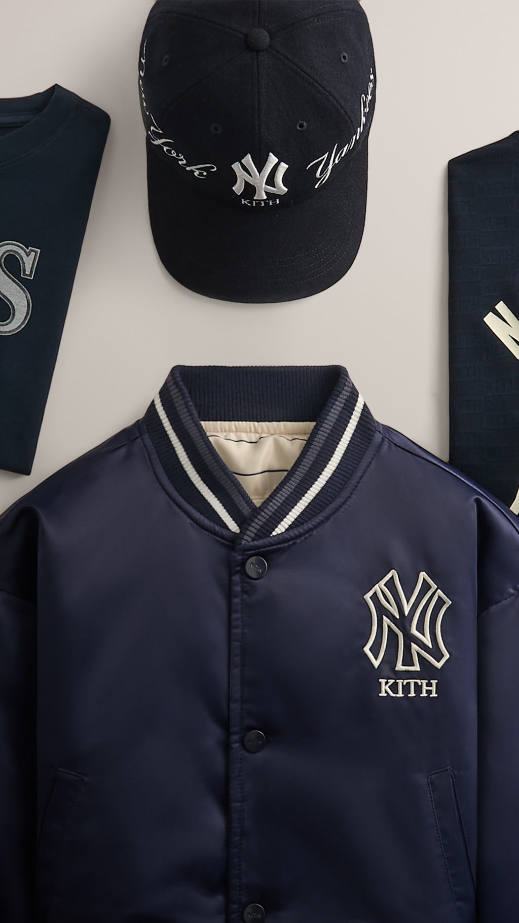 Kith for New York Yankees satin bomber jacket with embroidered NY logo, shown with wool cap and folded graphic tees, close mobile crop