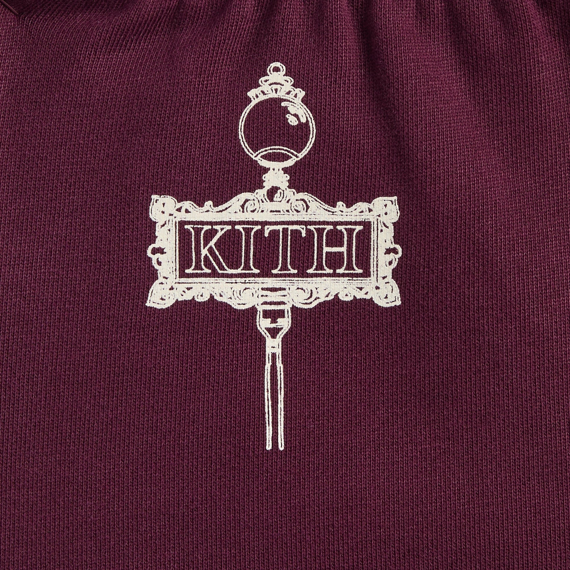 Close-up of ornate cream Kith storefront sign graphic on burgundy Kith Baby Logo Nelson Short