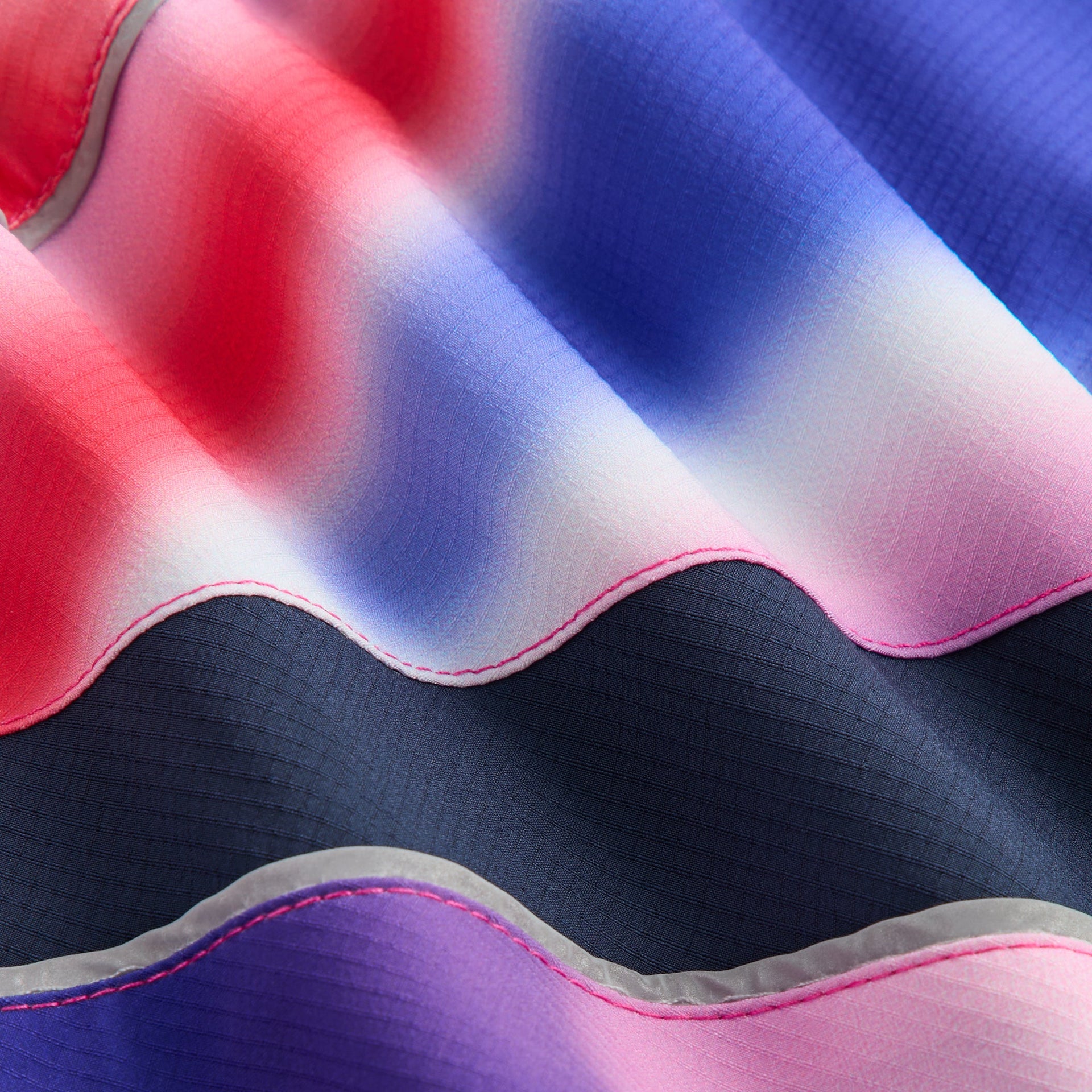 Kith Kids Lora Windbreaker fabric close-up of ripstop Tempo swirl print with navy panel and reflective piping