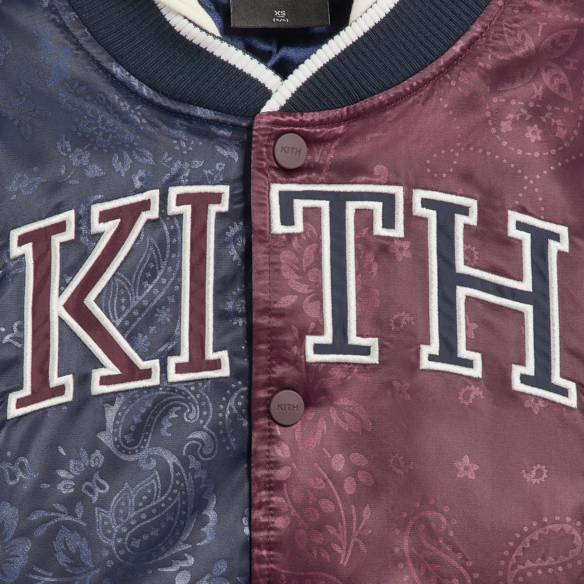 Kith Kids Gorman Jacket close-up of KITH varsity applique and snap buttons on navy-to-burgundy paisley satin