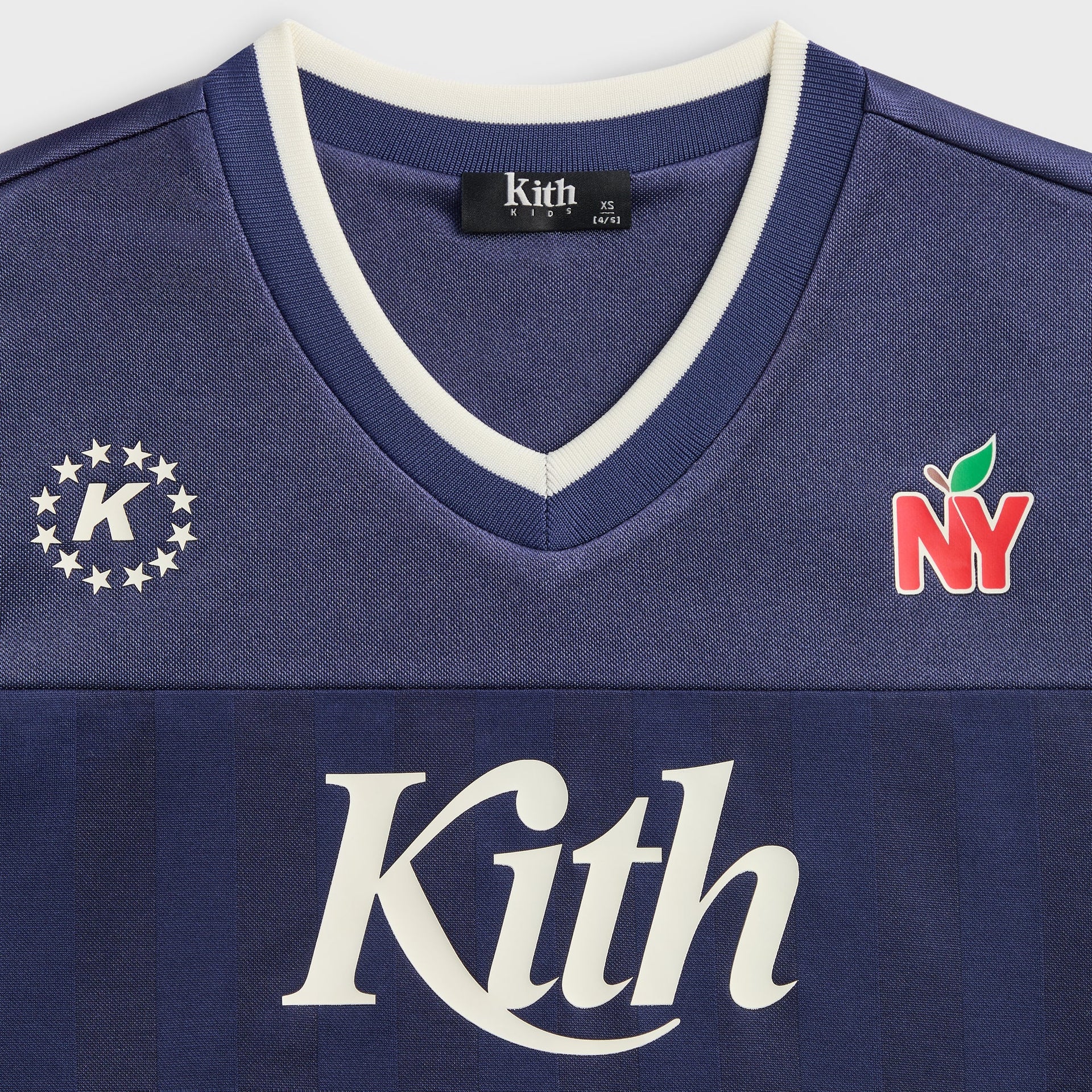 Kith Kids Malik Jersey in navy nocturnal, close-up of cream V-neck trim, star crest, NY apple and Kith logo