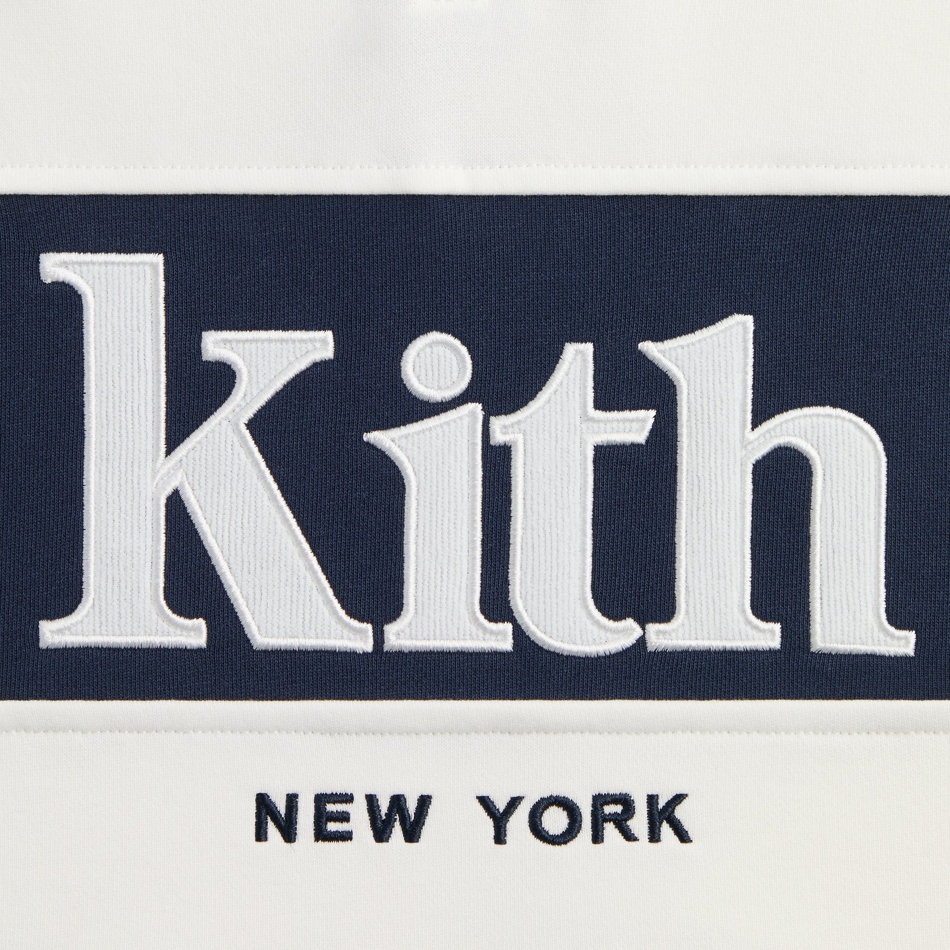 Close-up of white Kith New York embroidery on navy chest panel of cream Kith Kids Nelson Collared Pullover