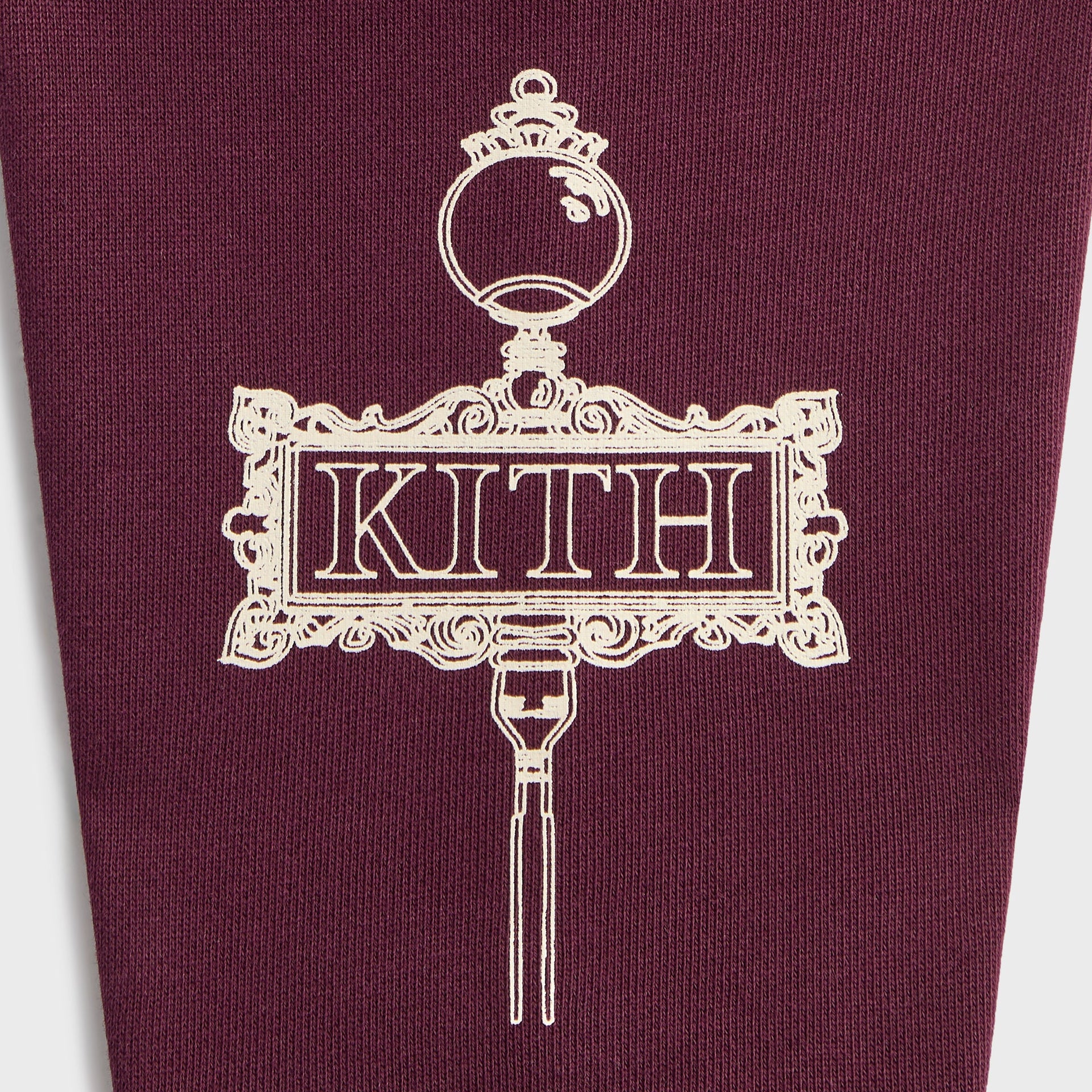 Kith Kids Hunter Pullover close-up of cream ornate Kith street sign sketch on burgundy fabric