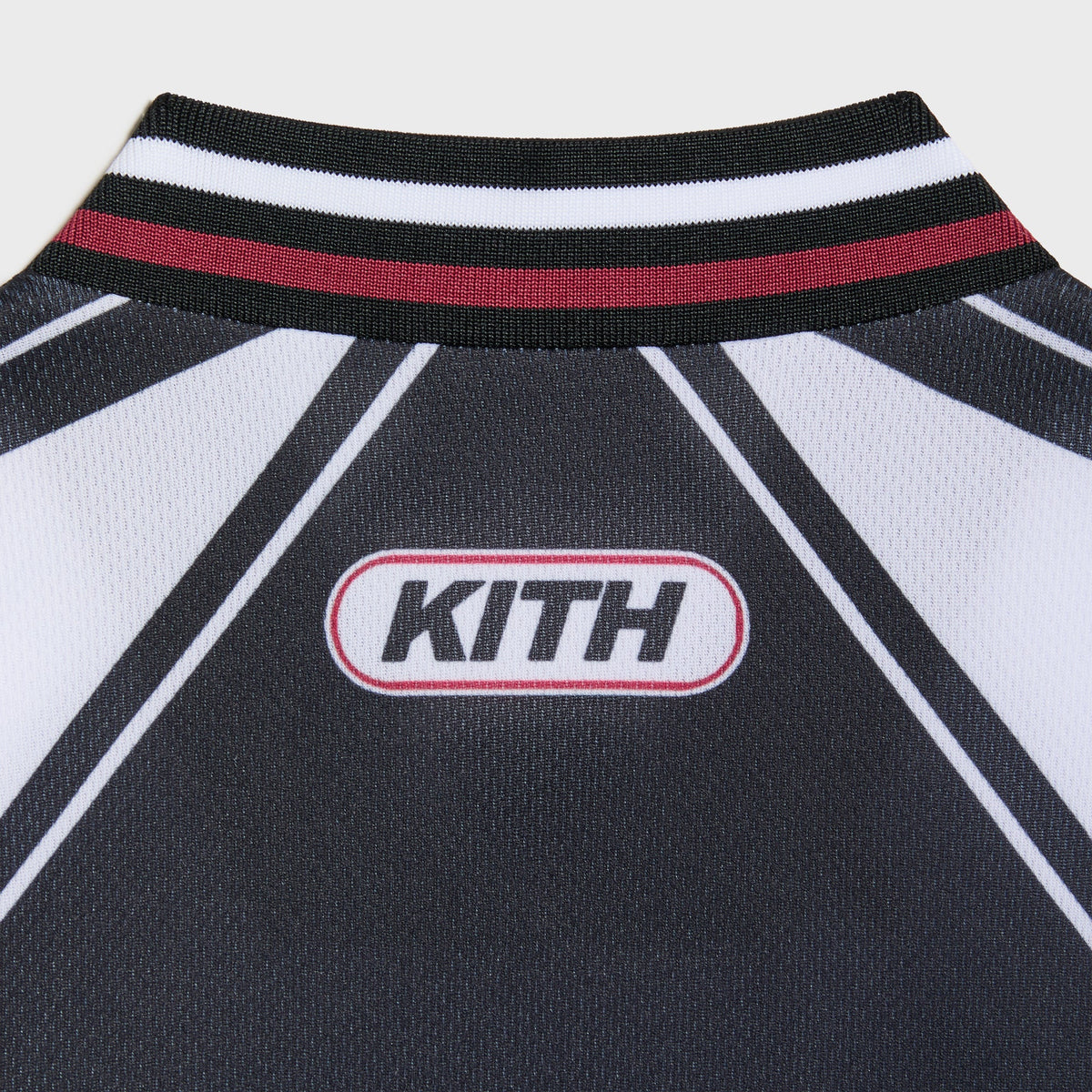 Close-up of the black Kith Kids Moto jersey back collar with white KITH oval patch on red and white ribbed trim