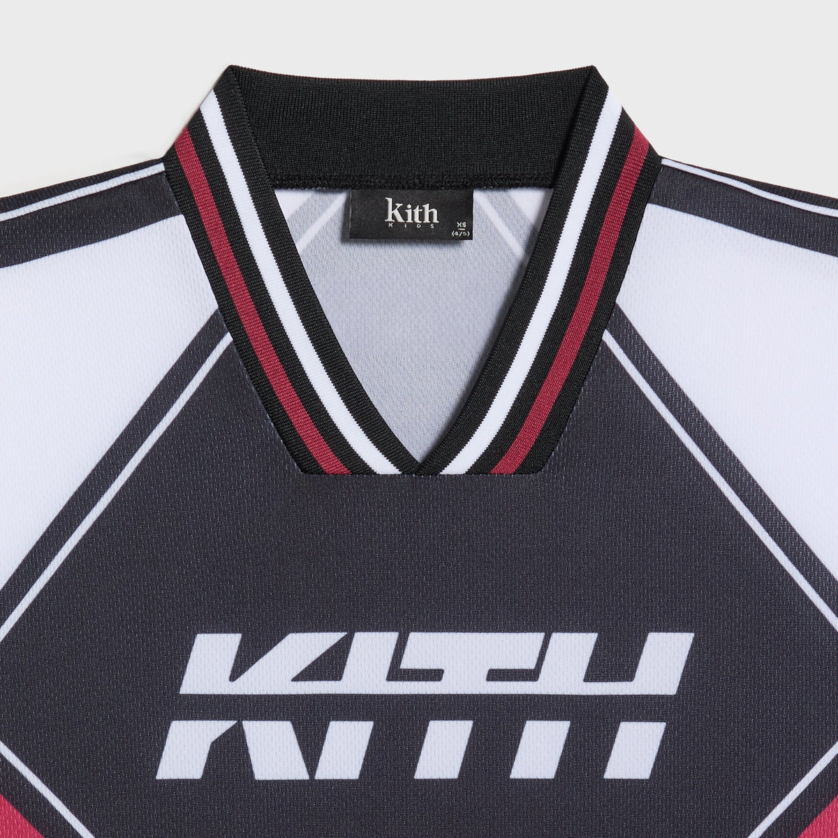 Close-up of the black Kith Kids Moto jersey V-neck collar with red, black and white ribbed trim and white KITH chest logo
