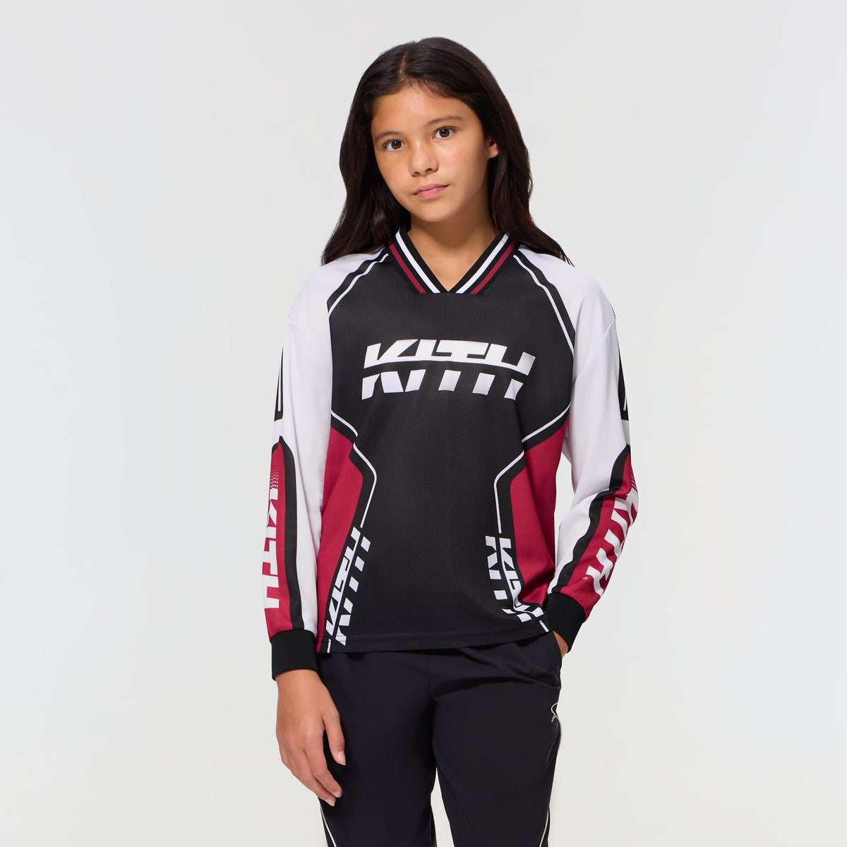 Child wearing the black Kith Kids Moto Mesh Donovan long-sleeve jersey tee, front view with red and white motocross-style paneling