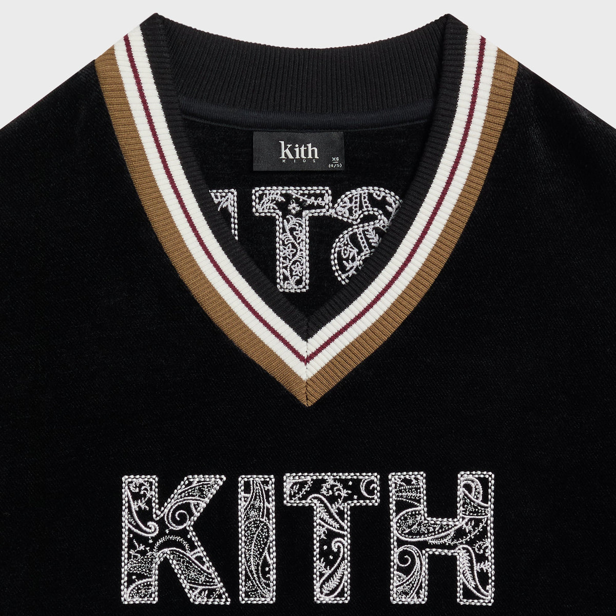Close-up of the black Kith Kids V-Neck sweatshirt collar with tan, white and burgundy cricket-stripe ribbed trim