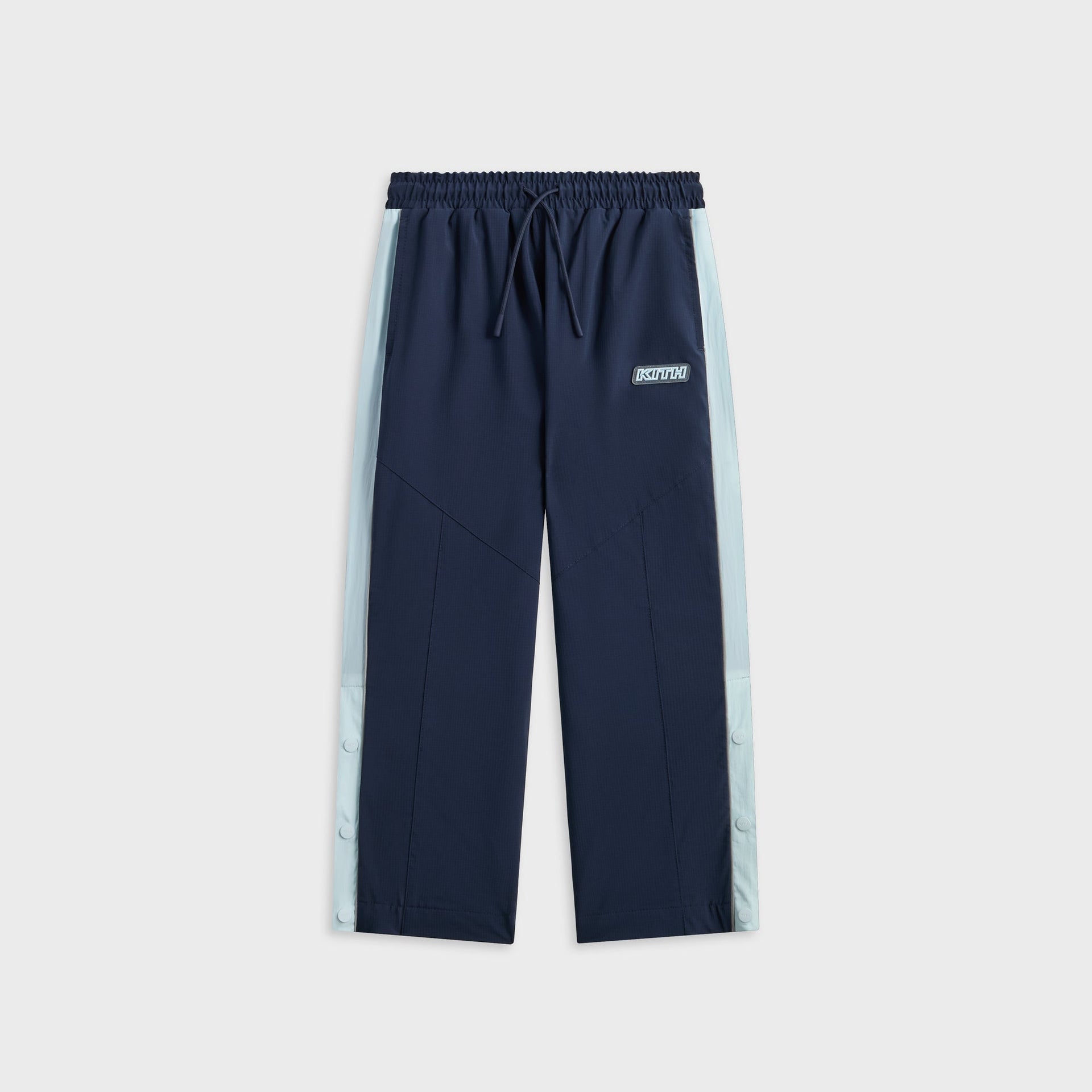 Kith Kids Lora Track Pant in navy, front flat lay with light blue snap-button side stripe and KITH rubber patch