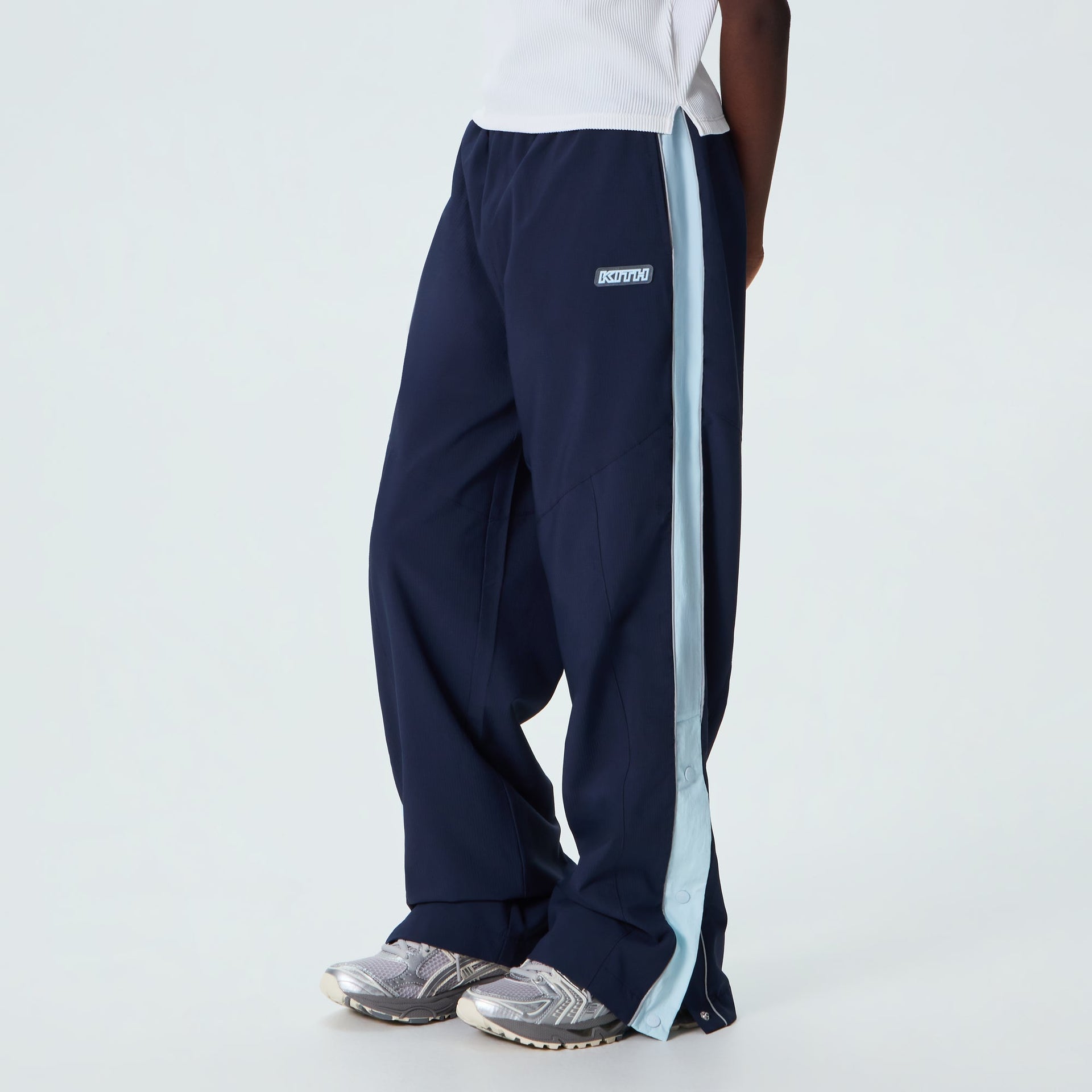 Kith Kids Lora Track Pant in navy worn on model, side view showing light blue tearaway side stripe and sneakers