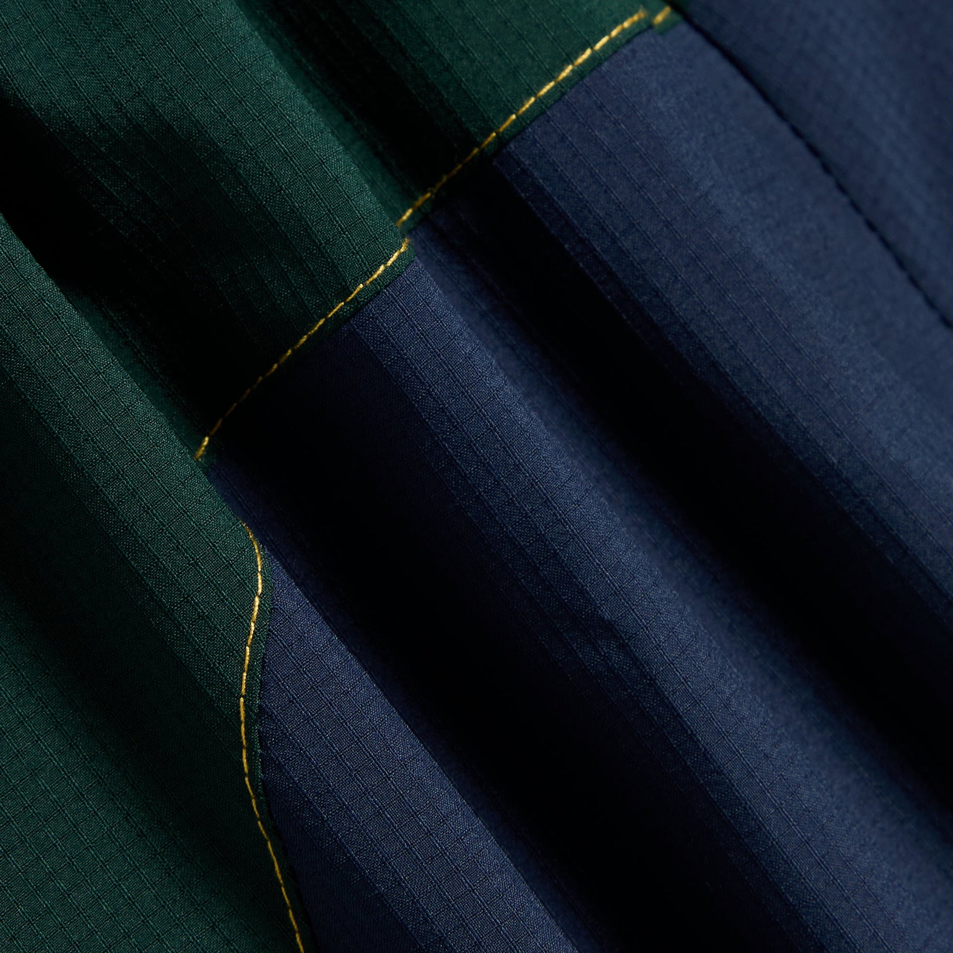 Close-up of the green and navy ripstop panels with gold topstitching on the Kith Kids Milo track pant