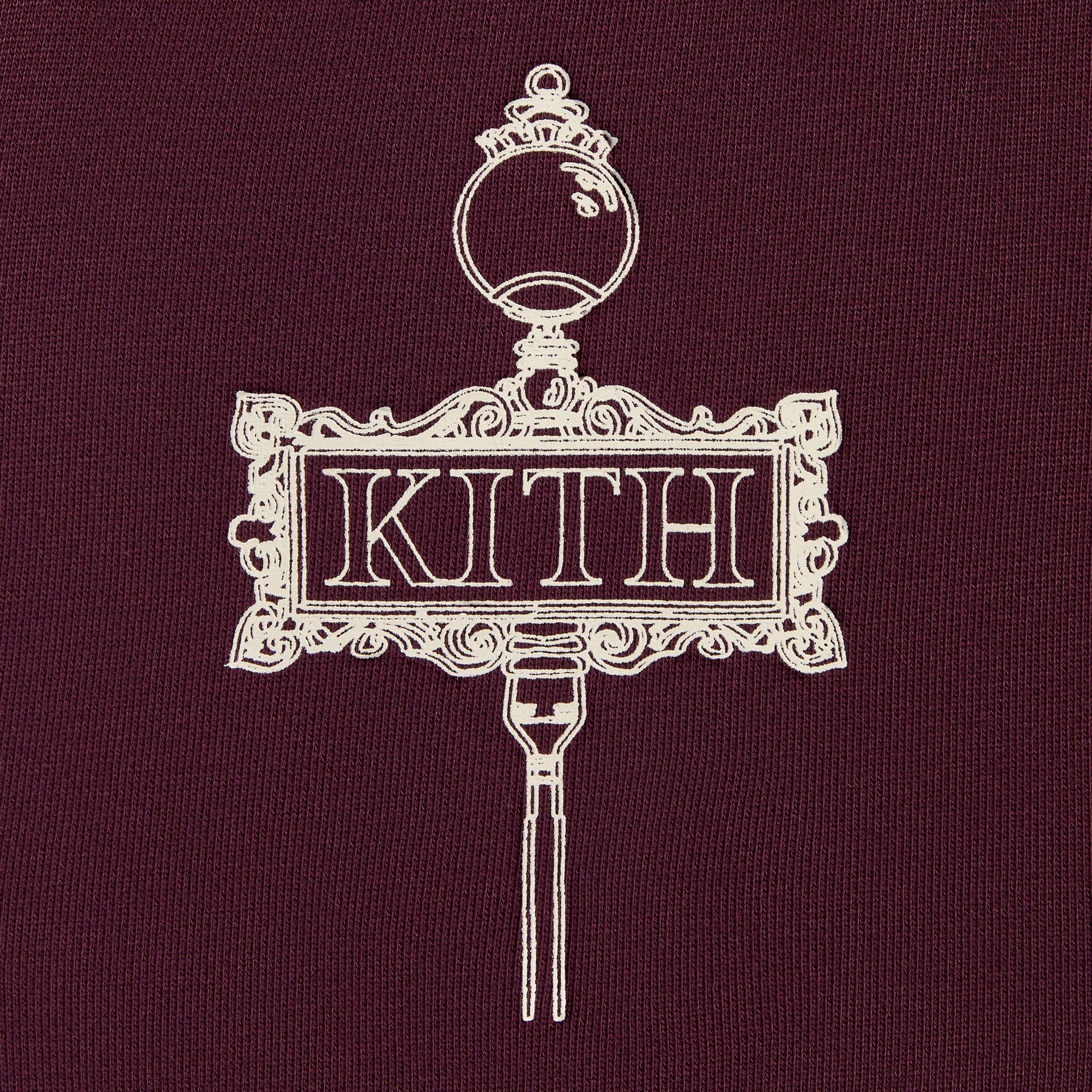Kith Kids Logo Nelson Short in burgundy essence, close-up of cream Kith ornamental lamppost sign graphic