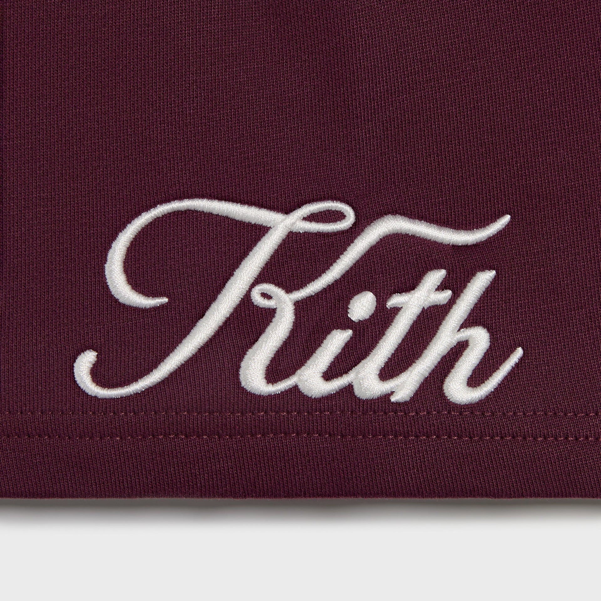 Kith Kids Logo Nelson Short in burgundy essence, close-up of embroidered white Kith script logo at hem