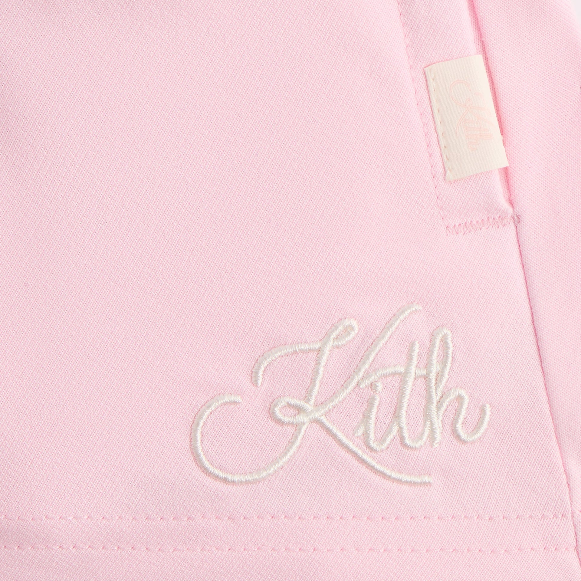 Close-up of the white cursive Kith embroidery and woven tag on the pink Riley II skort