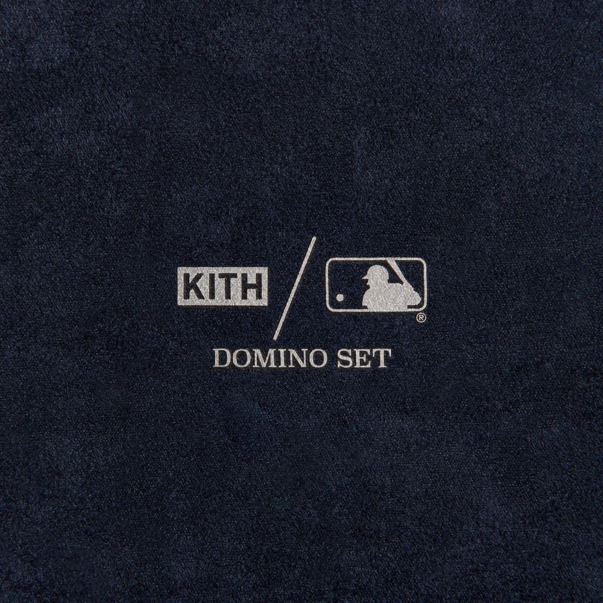 Close-up of the embossed cream NY logo patch on the domino case's navy leather exterior