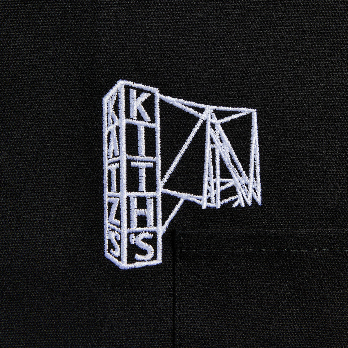 Close-up of white line-art Kith wireframe scaffold graphic embroidered above the apron's front pocket