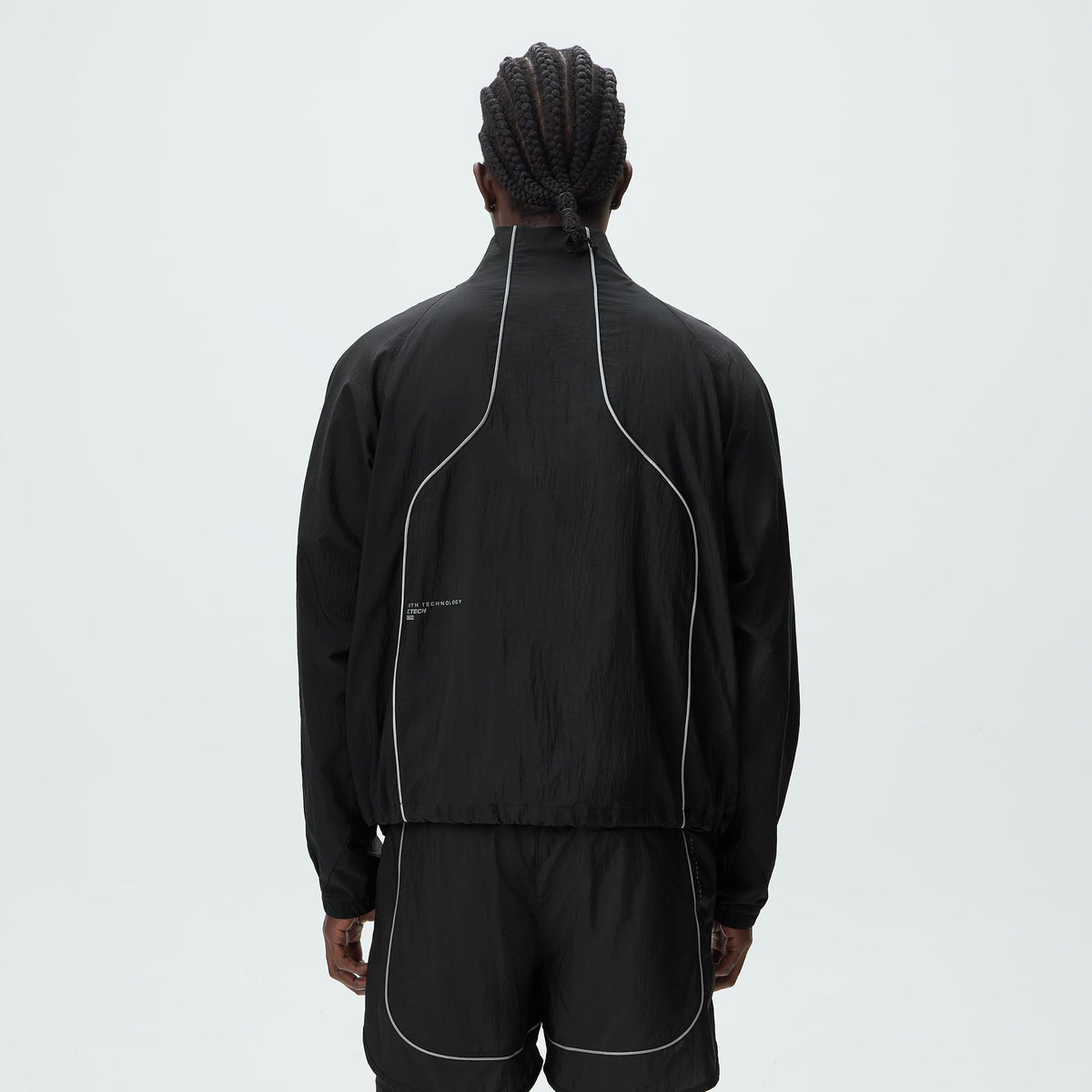 Man modeling Kith Eryx Track Jacket in black, back view showing raglan seams and piping