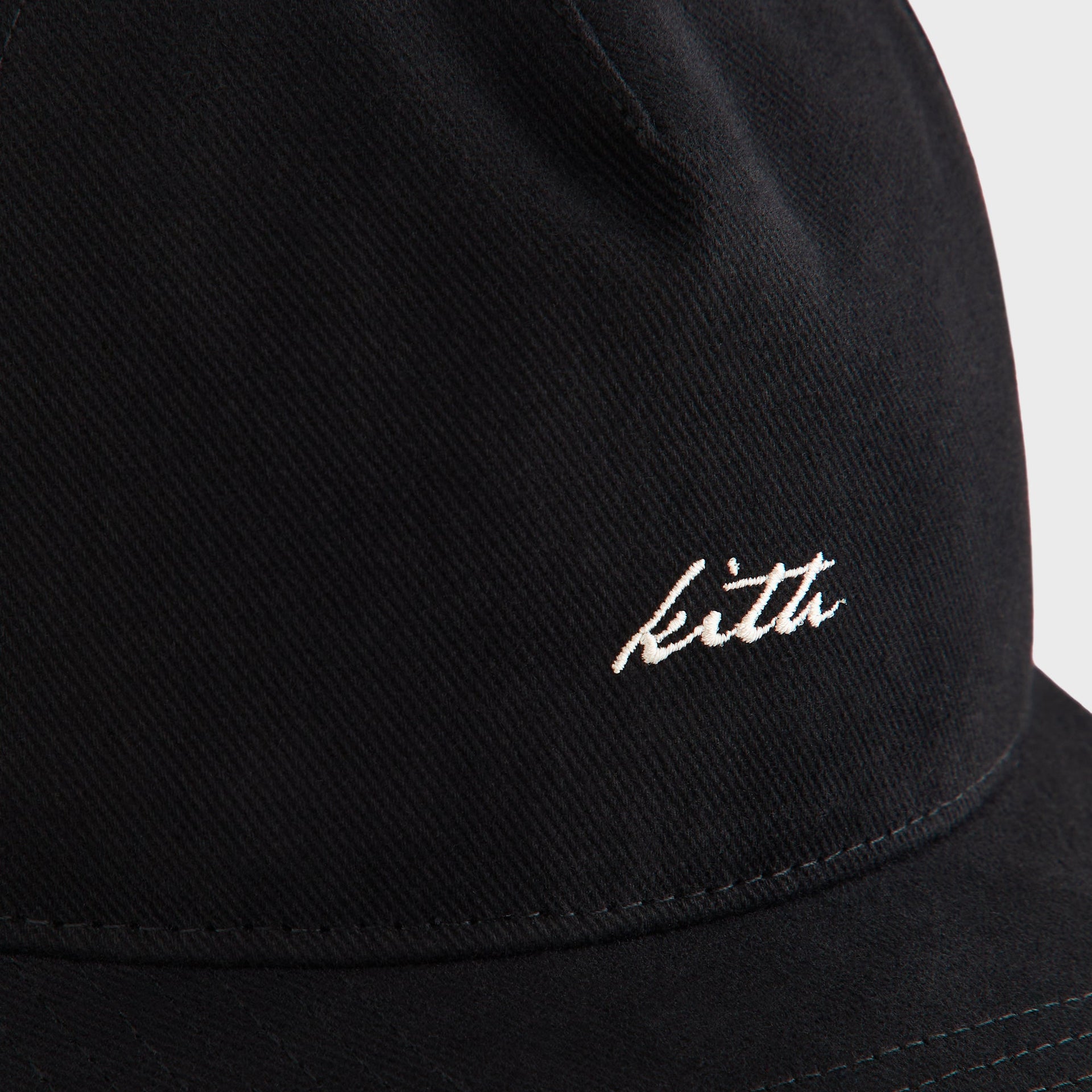 Close-up detail of white Kith script embroidery on the brushed twill crown of the black Low Pinch Crown Cap