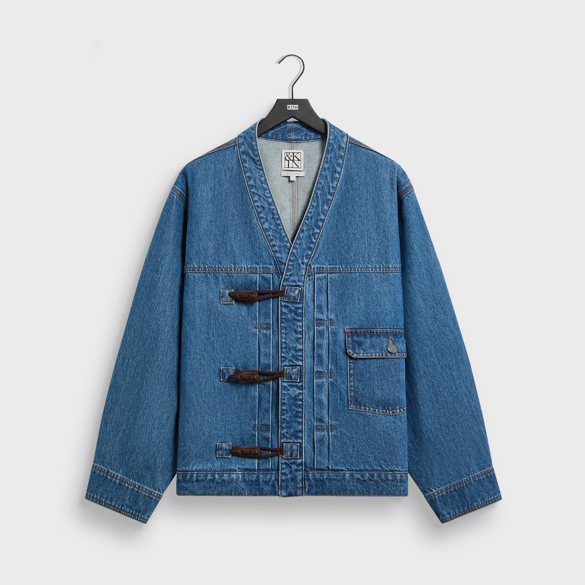 &Kin Denim Clint Trucker Jacket in River Indigo, front view on hanger, collarless V-neck with brown toggle fastenings and chest pocket
