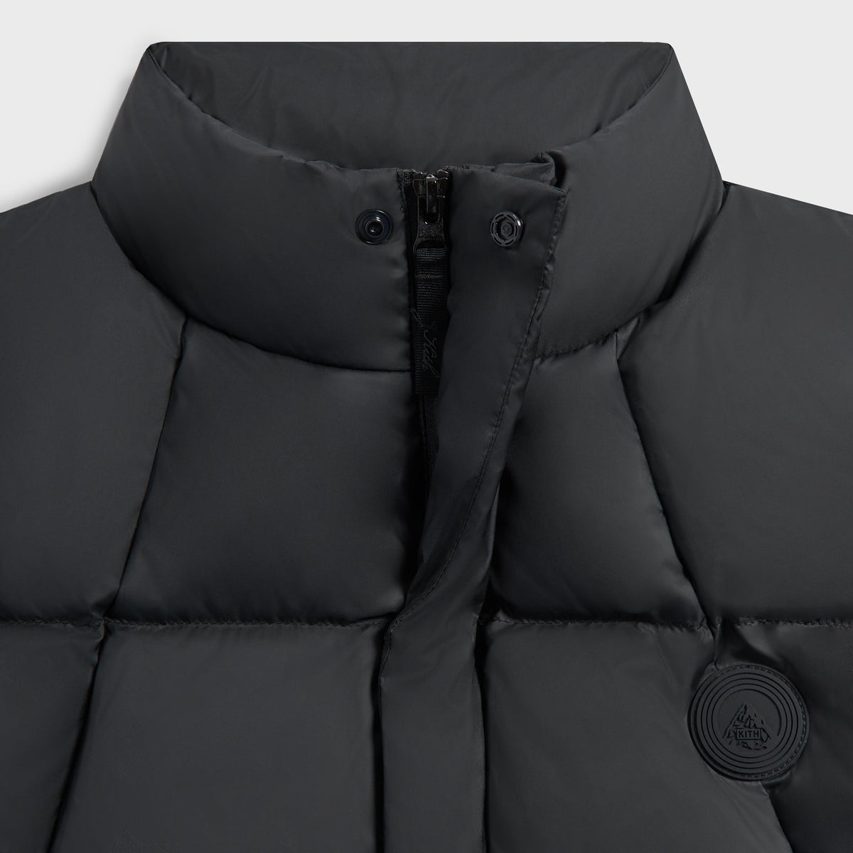 Close-up of the collar, zip and tonal badge on the black Matte Taffeta midi puffer vest